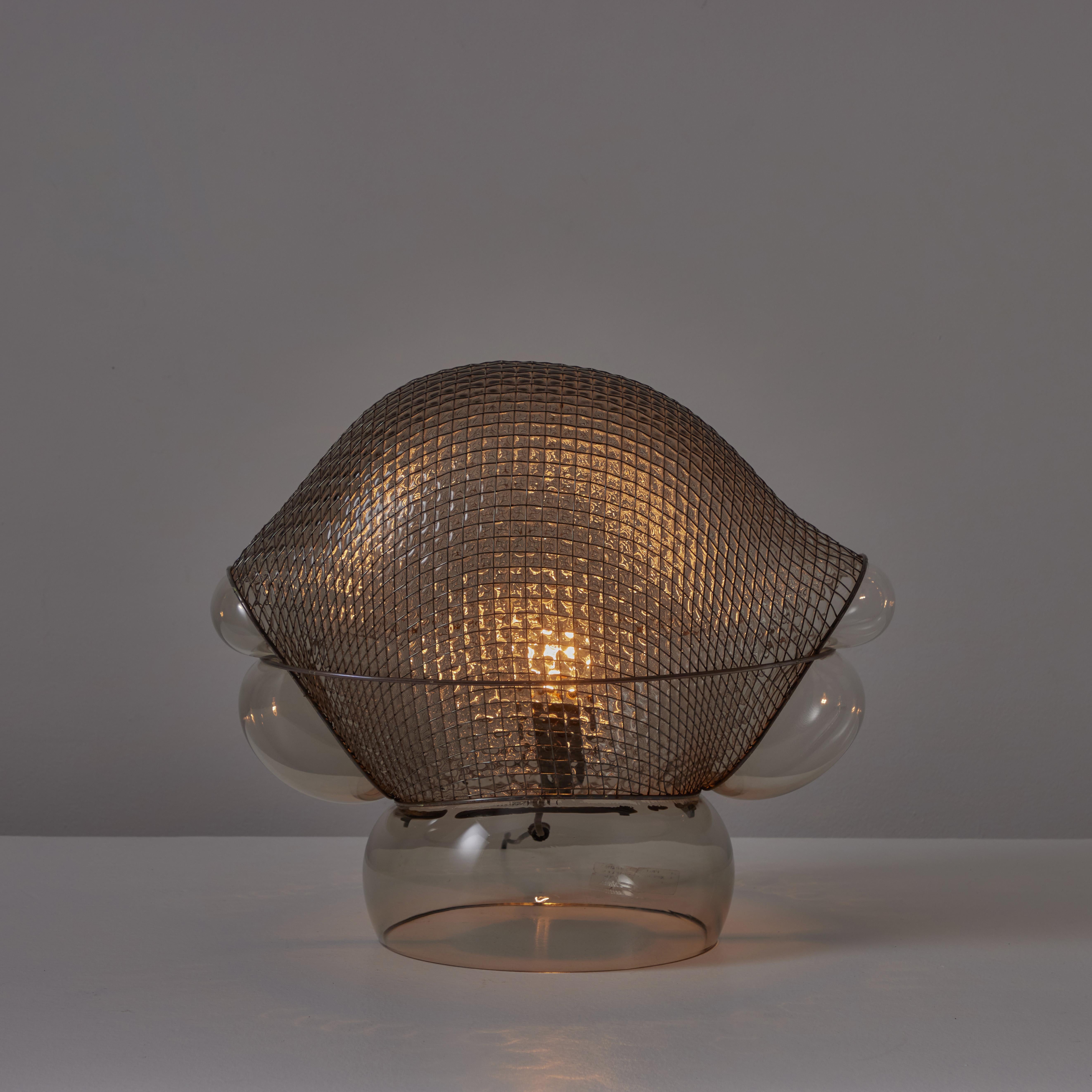 Patroclo table lamp by Gae Aulenti for Artemide. Originally designed in 1975. Smoke colored blown glass and steel mesh. Toggle switch on cord. Maintains original Artemide label. Holds a single E27 socket, adapted for the US. We recommend one 60w