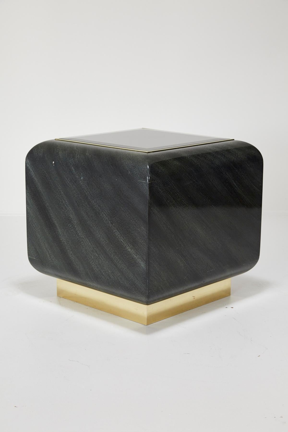Beautiful oversized cube shaped side or end table with soft rounded edges with Postmodern styling. Brass toe kicks support a rounded cube body covered in patterned black on dark green laminate. Top centre with beveled black glass insert with brass