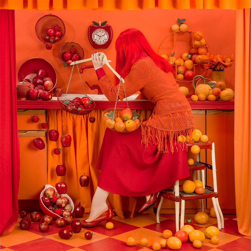 Patty Carroll Figurative Photograph - Apples and Oranges - Limited Edition, Fruit, Kitchen, Red, Woman, Interior