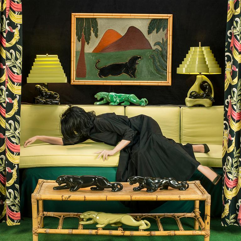 Panther is a color photograph of a staged panther themed room, created by photographer Patty Carroll. This scene consists of a mannequin, representing a woman, laying on a couch surrounded with eclectic color coordinating decor. Panther is from