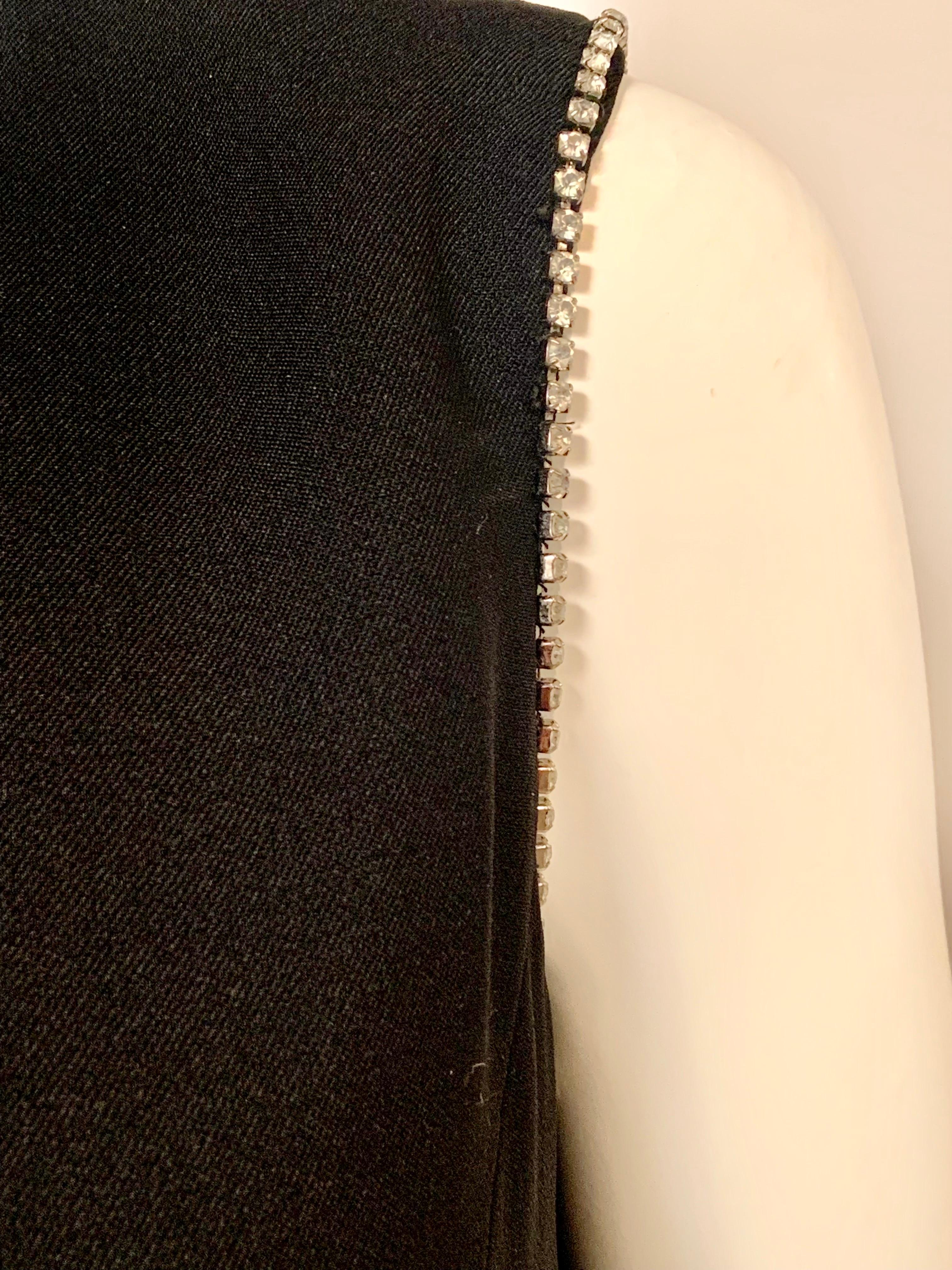 Dieses in Amerika hergestellte Kleid aus den 1960er Jahren von Pattullo-Jo Copeland ist sehr elegant und hat ein sehr interessantes Design.  Die beiden Armlöcher und die linke Rocköffnung sind mit Strasssteinen verziert.  Das schwarze Wollkleid hat