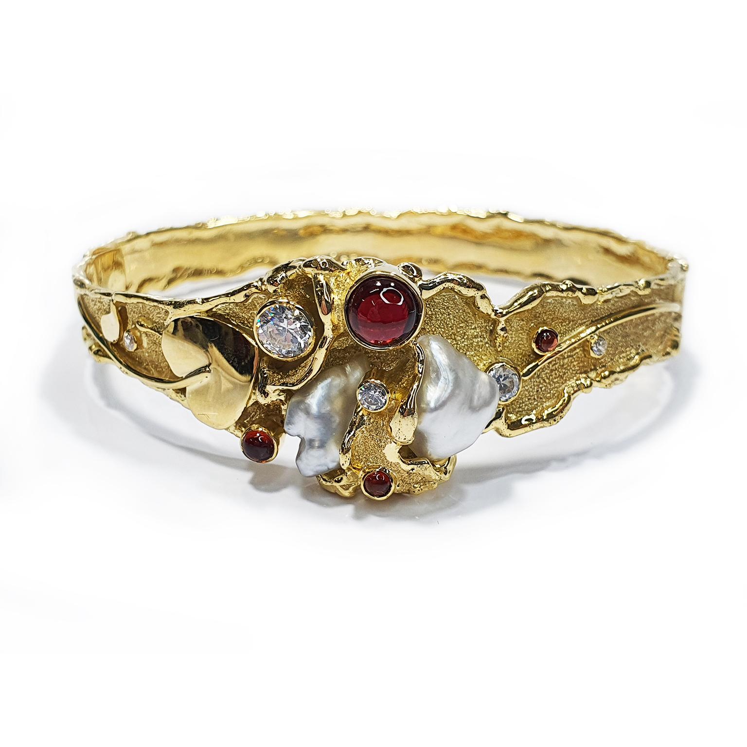 Paul Amey’s signature molten edge bangle is crafted from 9K yellow gold with garnets, leaf and vine motif and Keshi pearls. This molten edge garnet bangle contains a 12mm garnet cabochon, a 6mm garnet cabochon, a 4mm garnet cabochon and a 2.5mm