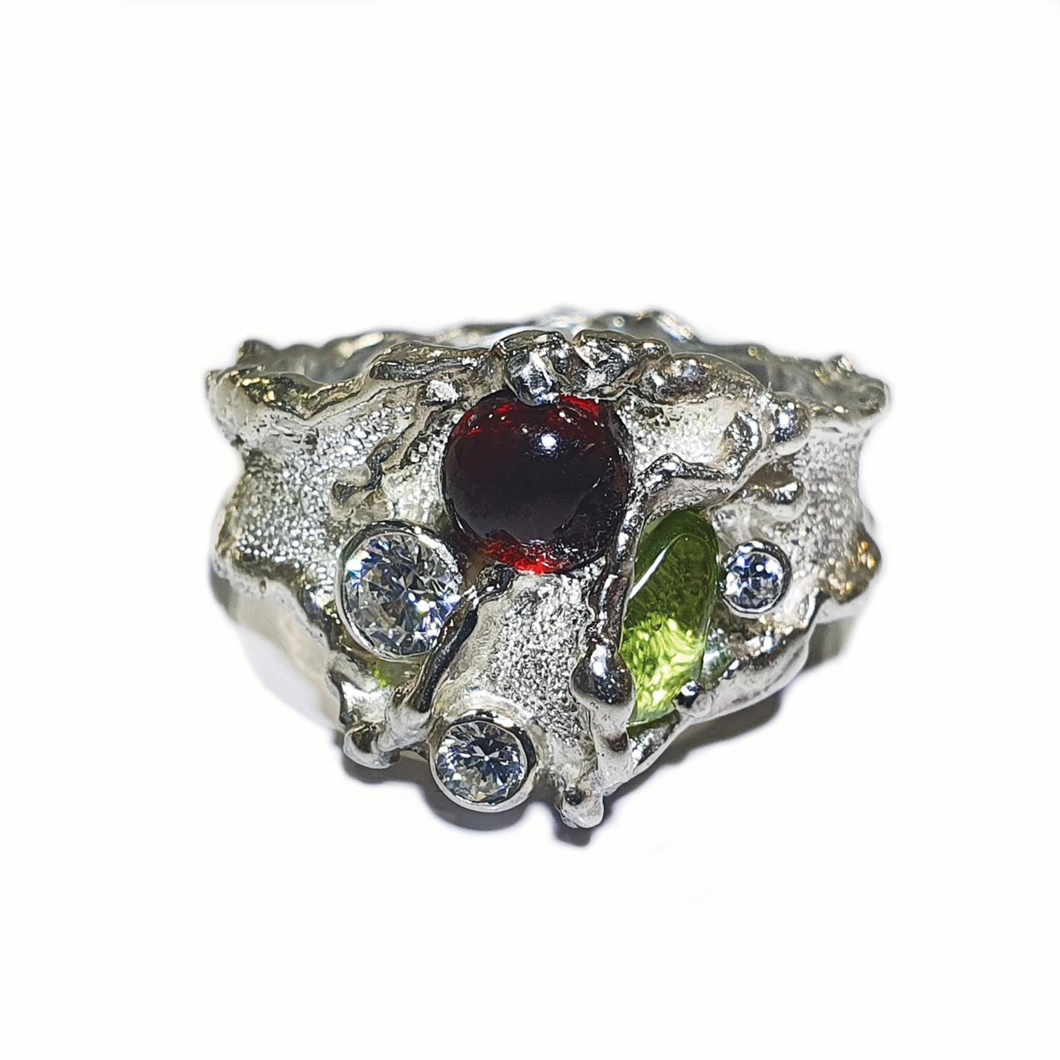 Paul Amey’s Molten Edge Sterling silver ring was crafted from tarnish resistant Sterling Silver. The ring features white Swarovski crystals, a natural peridot crystal and a garnet cabochon. The ring is finished with Paul Amey’s signature texture.