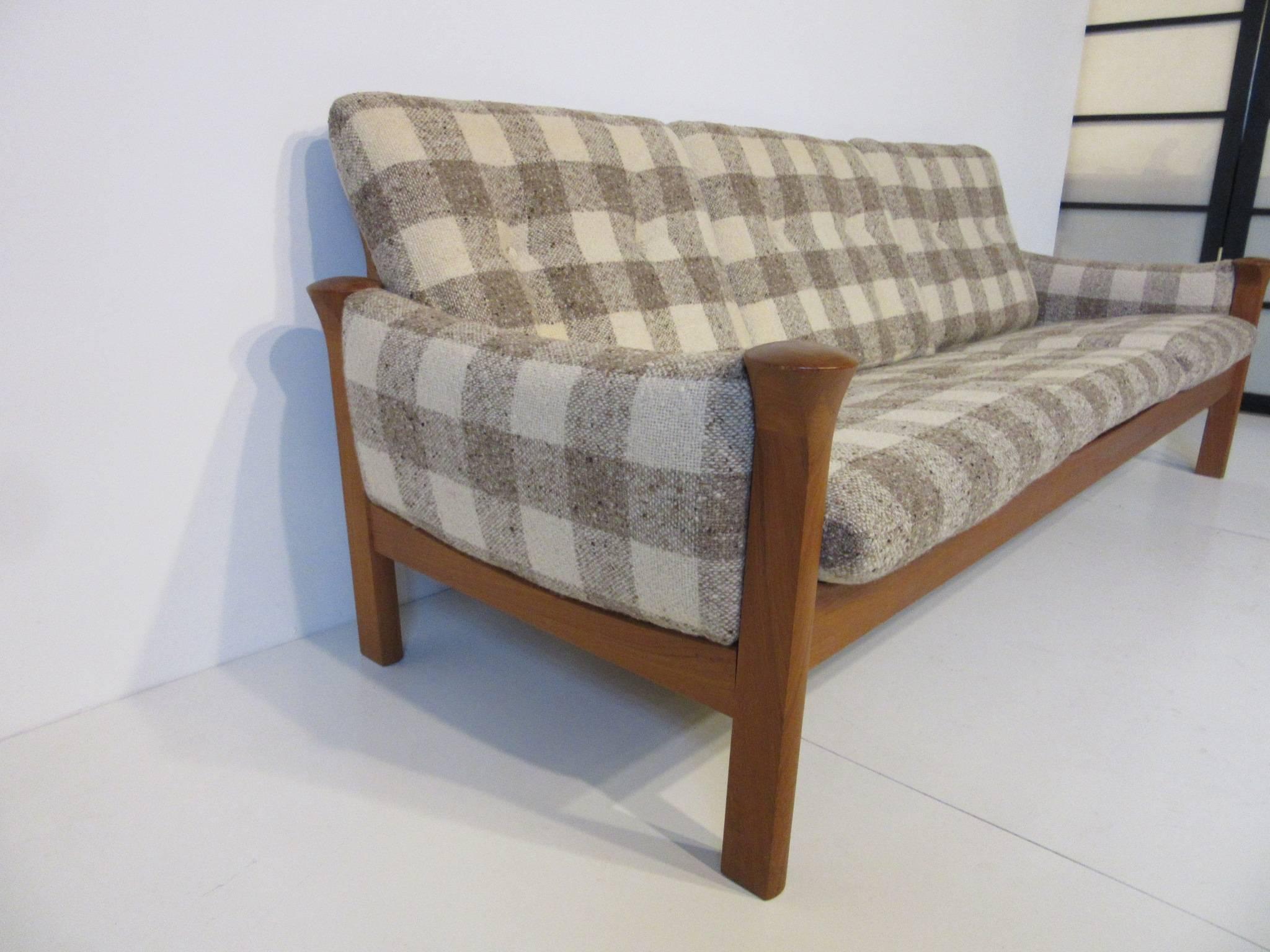 A teak wood sofa upholstered in a soft oat meal textured cream and mocha Buffalo plaid fabric, retains the manufactures tag by Cado made in Denmark.