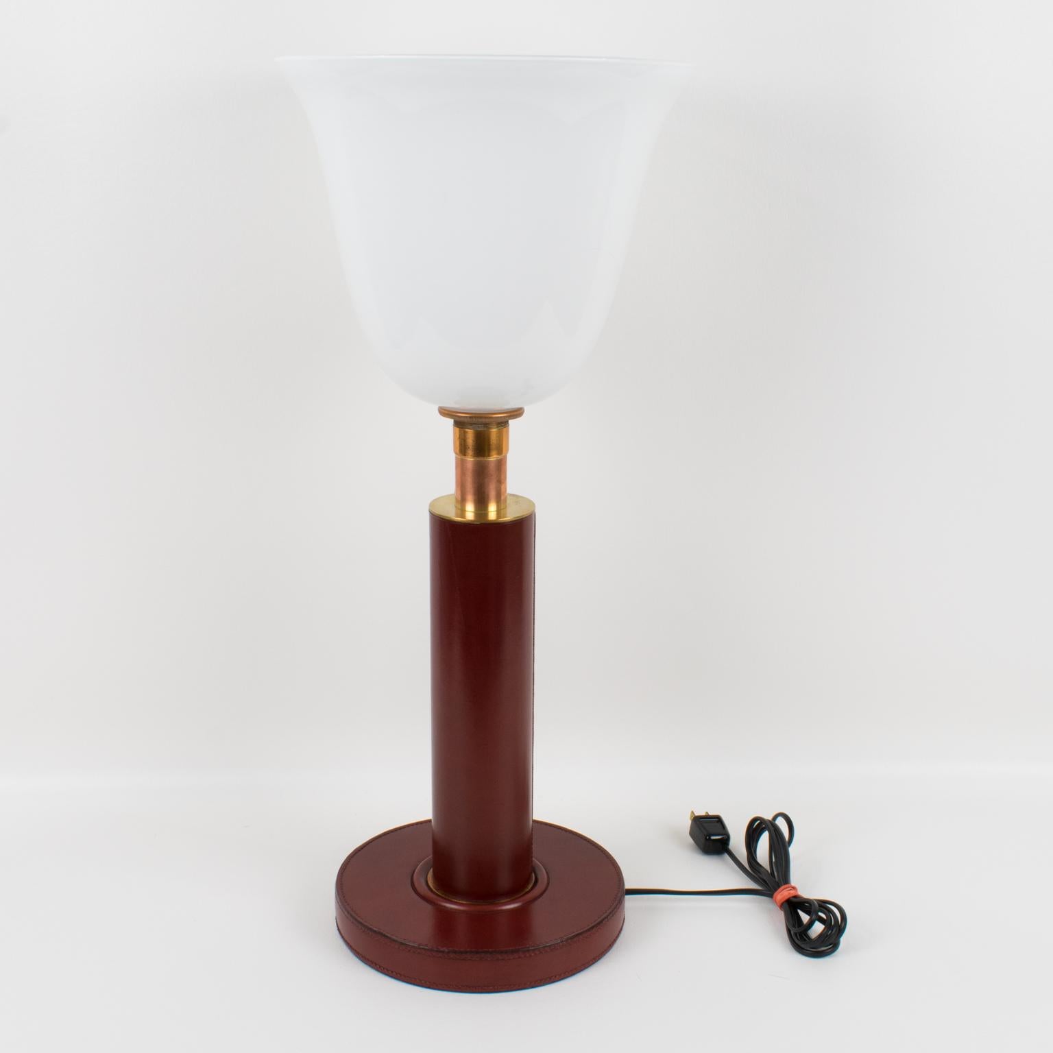 Stunning French Art Deco table lamp, by Paul Dupre Lafon, circa 1950. This elegant desk or table lamp features a hand-stitched oxblood red leather base and body with brass and copper accents. Upright lamp with white opaline glass tulip shade.