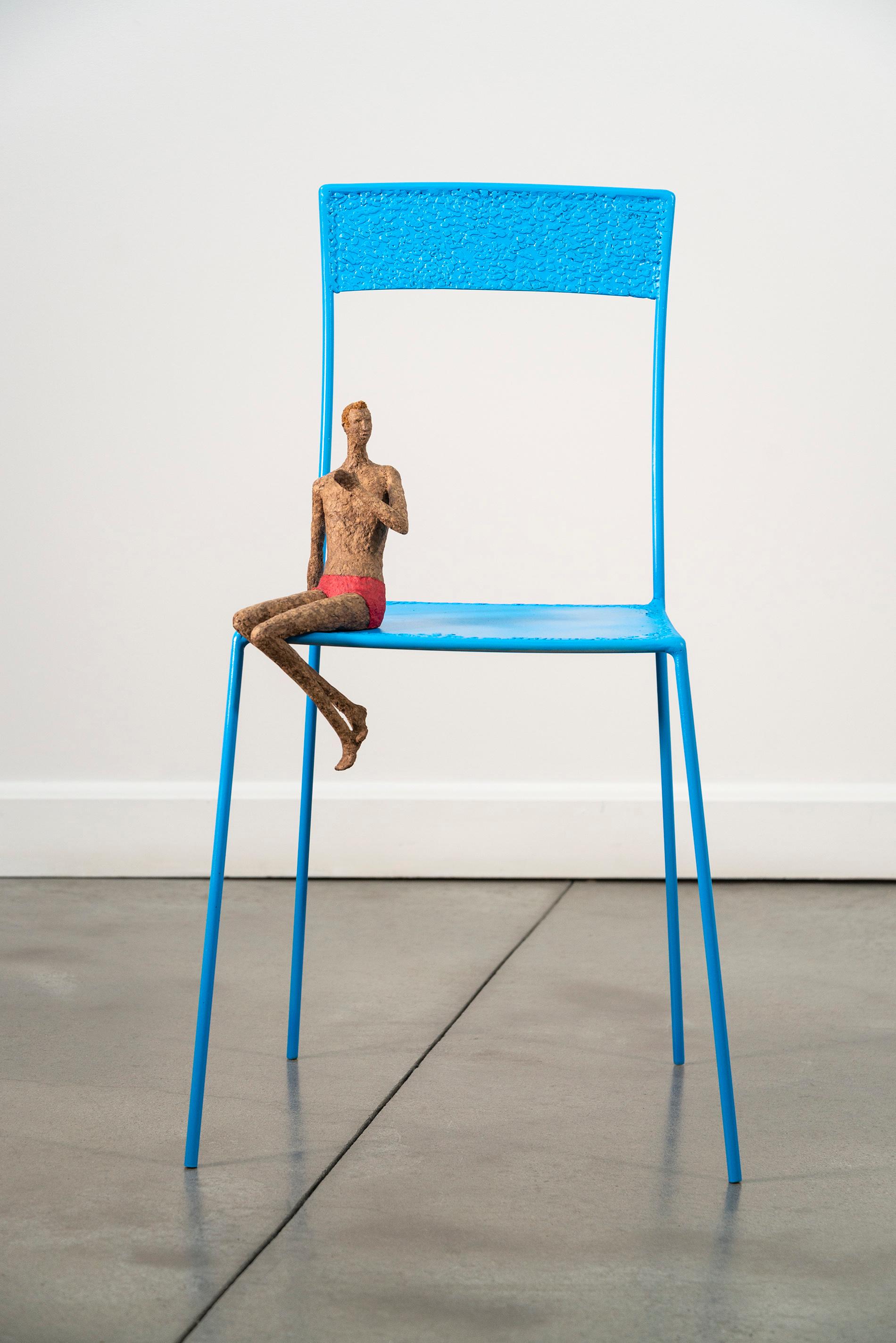 Equally fun and compelling, this new contemporary sculpture from Paul Duval immediately engages the viewer. On a large metal chair (la grande chaise) painted a bright blue, a figure sits, clad only in red shorts, leaning on one arm and gesturing