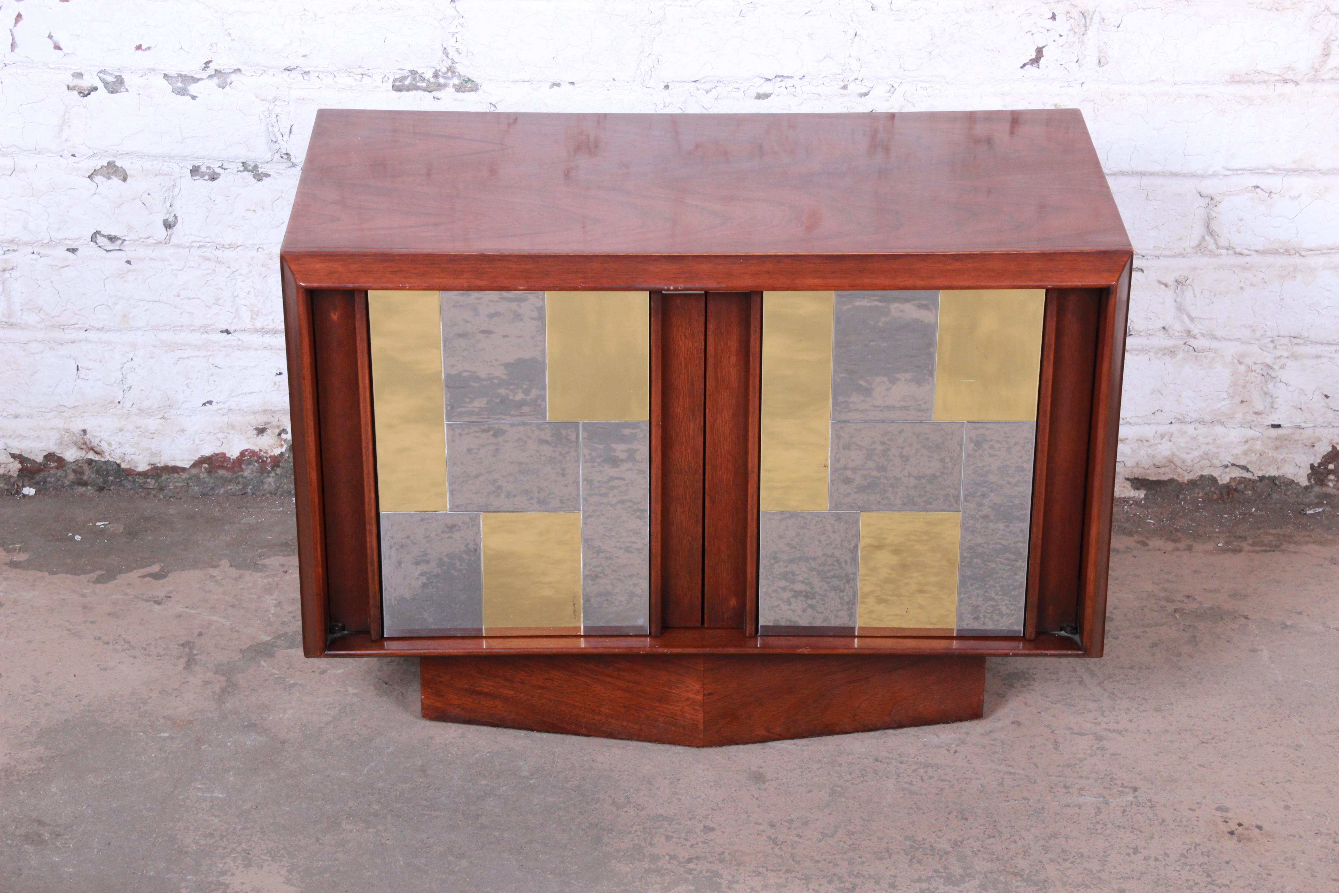An exceptional Mid-Century Modern cabinet or nightstand by Lane Furniture in the style of the Cityscape line by Paul Evans. The cabinet features gorgeous walnut wood grain, with a unique patchwork design in chrome and brass. It offers good storage,