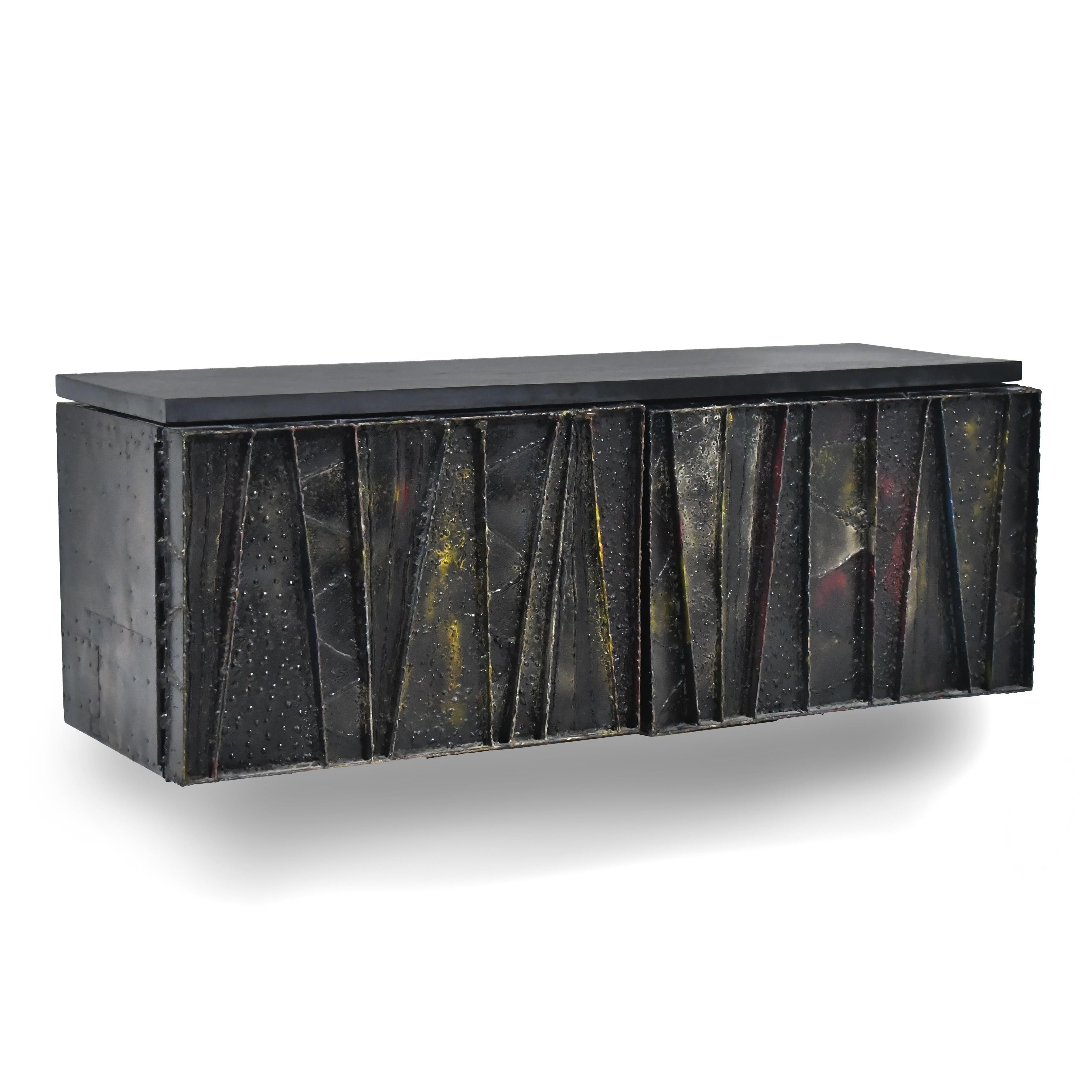 A sublime piece of functional sculpture by Paul Evans, this 1968 Deep Relief cabinet features a wall-mounted case with torch-cut, welded, polychromed and patinated steel doors concealing a shelf and topped with a piece of natural slate.

Hand signed