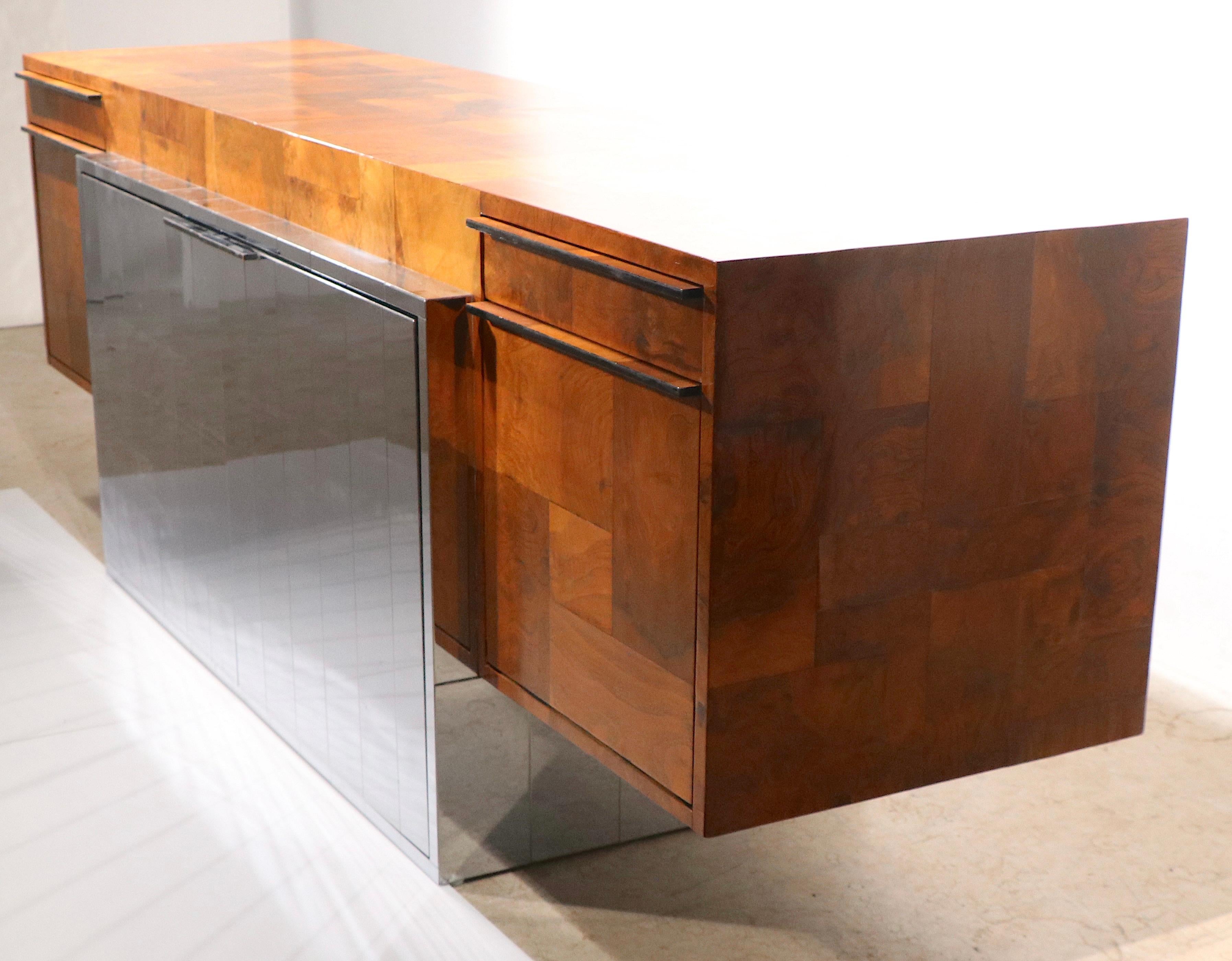 Spectacular Post Modern, Brutalist school credenza, designed by Paul Evans for Directional c. 1970's. The sideboard features a large rectangular cabinet with patchwork burl veneer, which is supported by a bright chrome patchwork center case. The