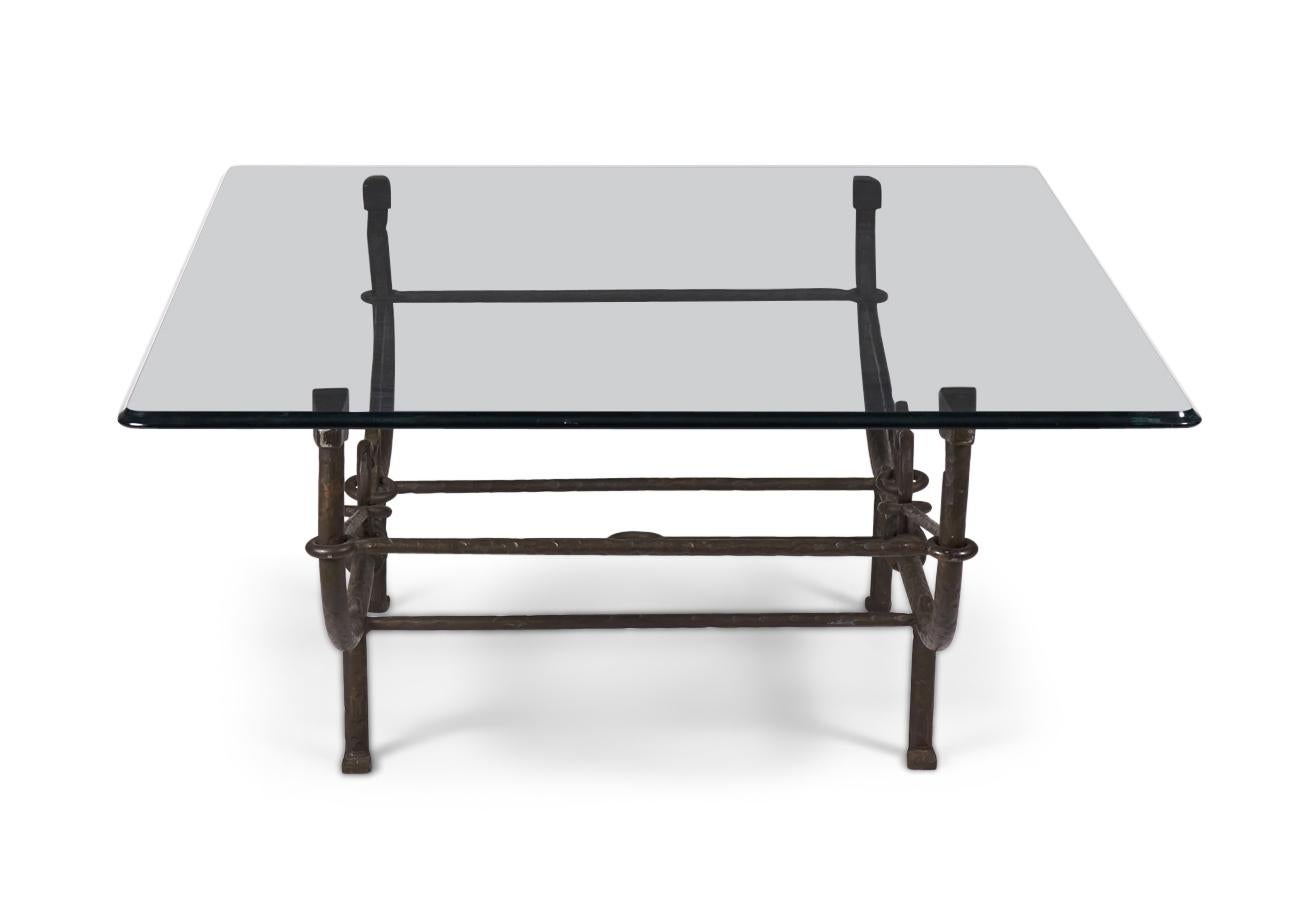 American Etruscan (circa 1980) forged and hammered iron frame coffee table with a stretcher base and curved arms that rise to support a plate glass table top (PAUL FERRANTE in the manner of DIEGO GIACOMETTI).
