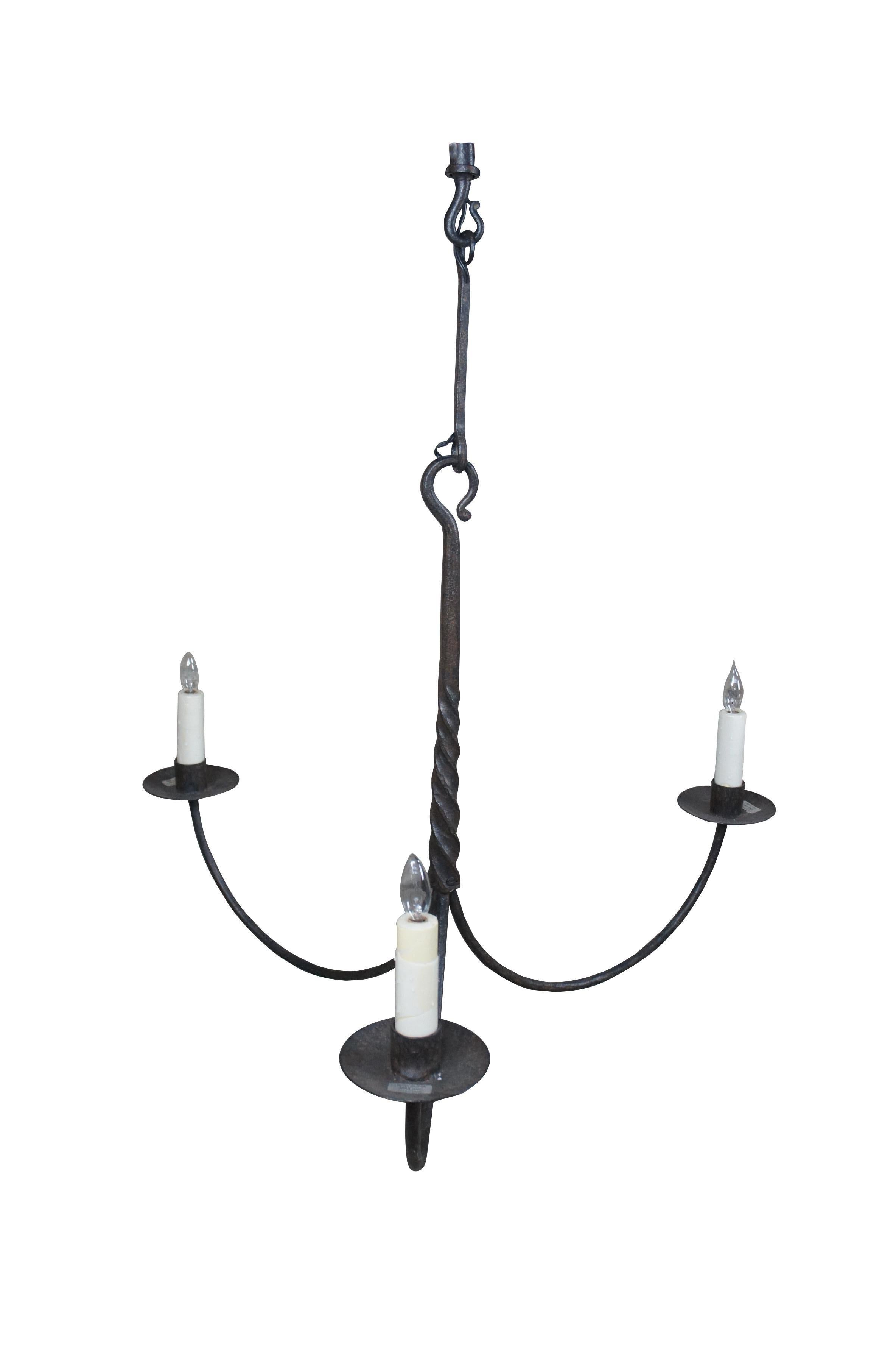 Paul Ferrante old iron forged wrought iron chandelier.  Features primitive old world styling with twisted center and down swept arms leading to three lights with wax drip pans and candle covers.

Paul Ferrante is a family-owned and operated company,