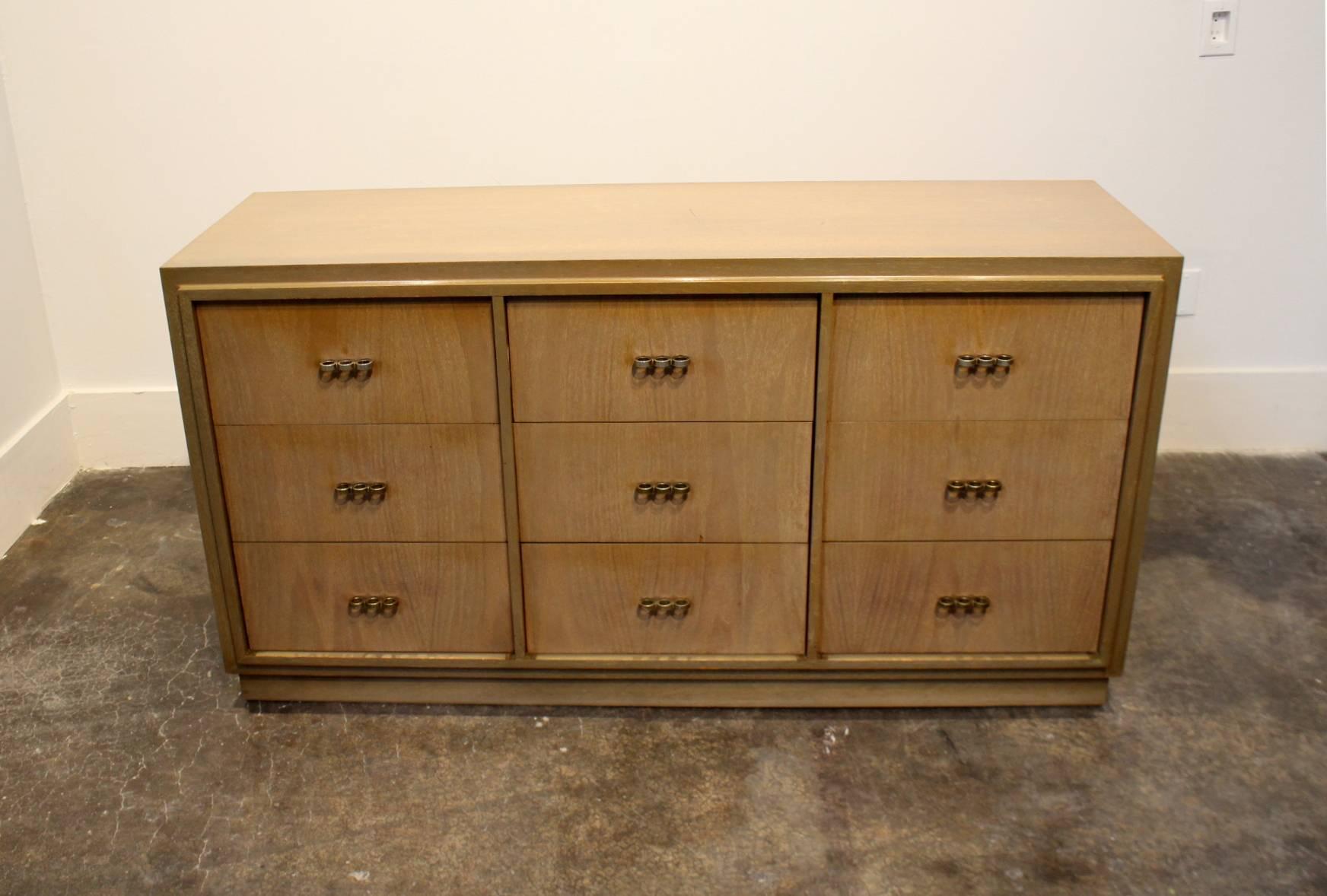 Striking sharp lines, beautiful walnut wood with olive green tones. Influences of Art Deco and Paul Frankl. Nine drawers total with brass-knuckle shaped pulls.

Matching nightstands available.