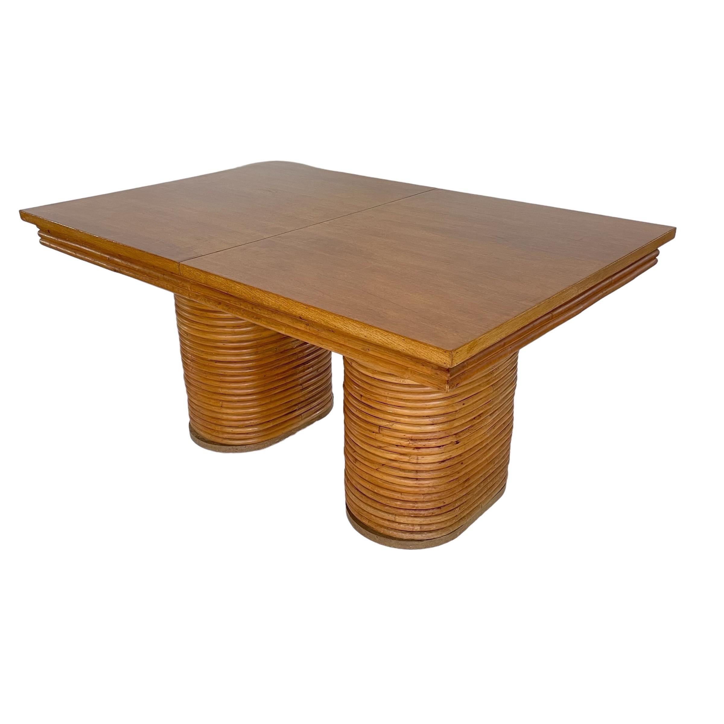 Tropical Mid Century Modern double pedestal extension dining table.  Rendered in rattan and wood, with two pedestals wrapped in stacked rattan supporting a three band stacked rattan top with a two part wood extension top and two additional leaves. 