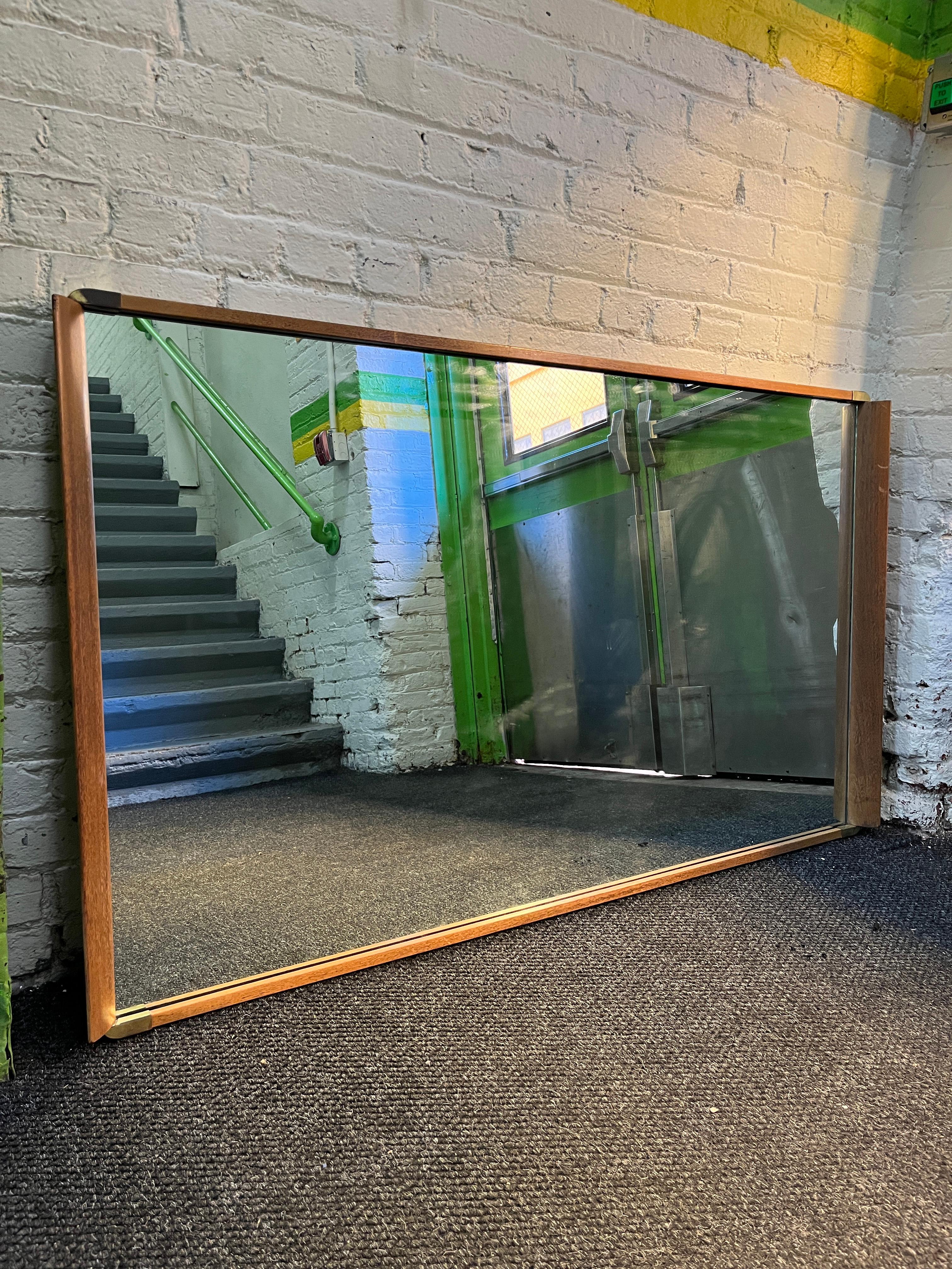 Un beau et grand miroir en noyer avec des accents en laiton par Paul Frankl. Miroir entouré d'un cadre en noyer et de coins en laiton. Miroir vendu à l'origine avec la commode 