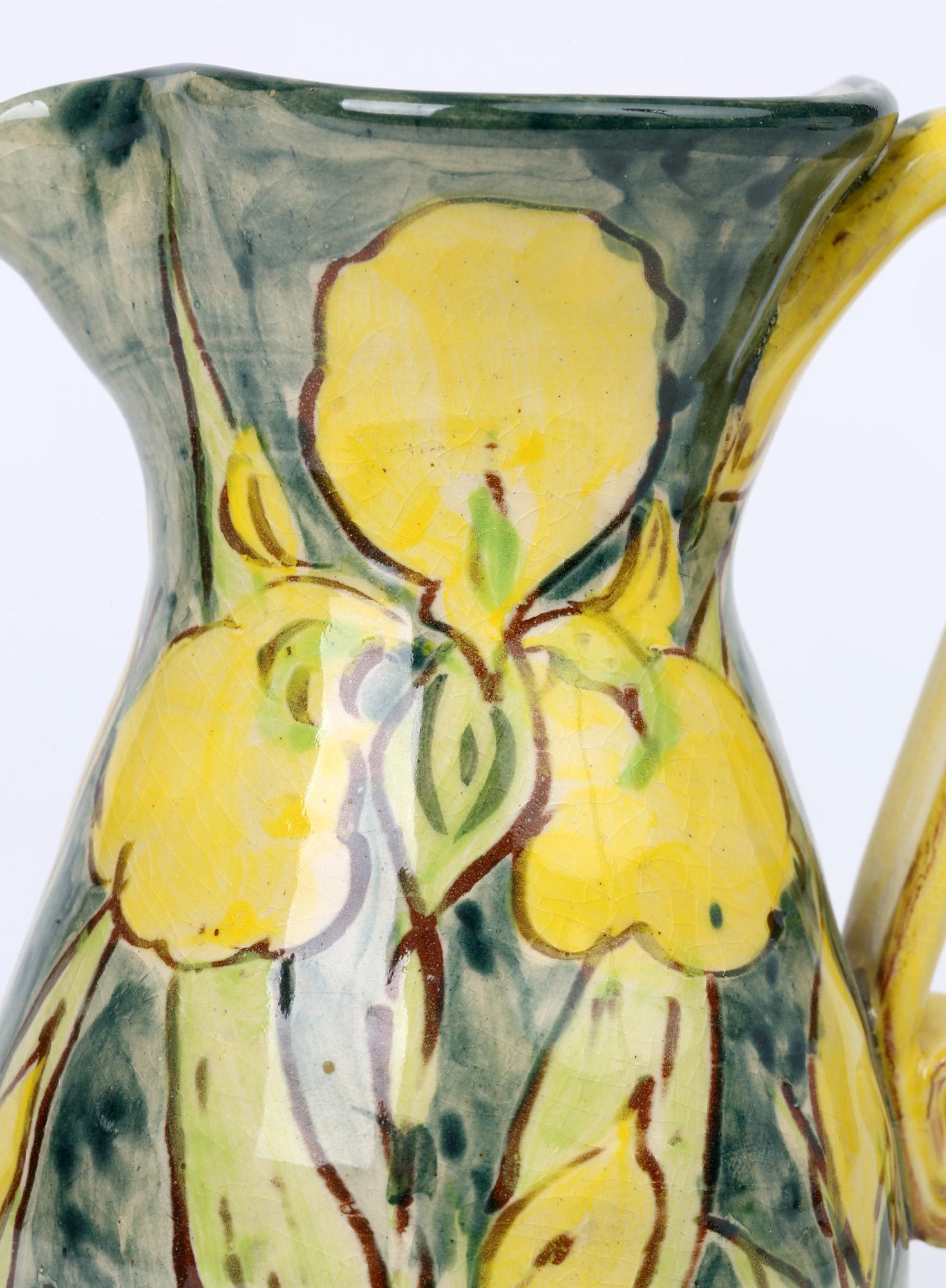 A stylish studio pottery jug hand painted in bright floral designs by Paul Jackson and dated 1993. The jug is handmade standing on a rounded base with a tall shaped rounded body and with an ear shape handle with coiled terminal and open shaped top