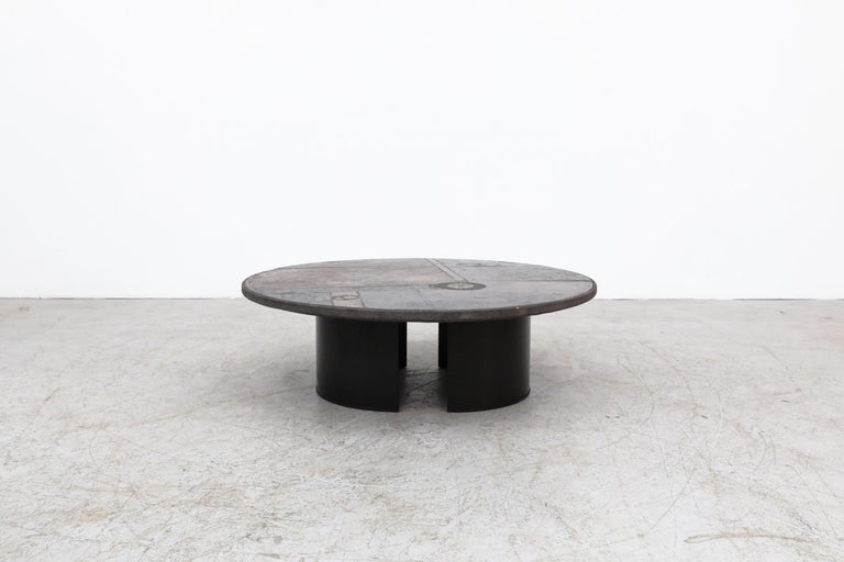 Brutalist round stone coffee table by Dutch designer Paul Kingma, 1970's, Netherlands. Made of thick concrete with inlaid stone, slate and other natural and mixed materials. The heavy top rests on two 1/2 round black enameled metal bases. Kingma's