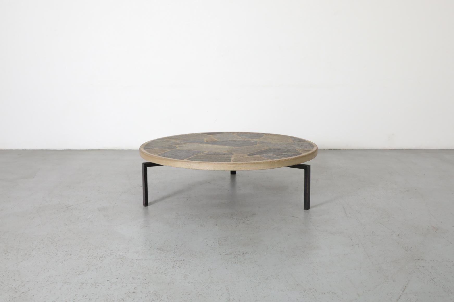 Mid-Century round black enameled coffee table with textured stone top. The base has three square tubular legs, and the stone top has a natural organic terrain. In original condition with visible wear, including chipping to the top and enamel loss on