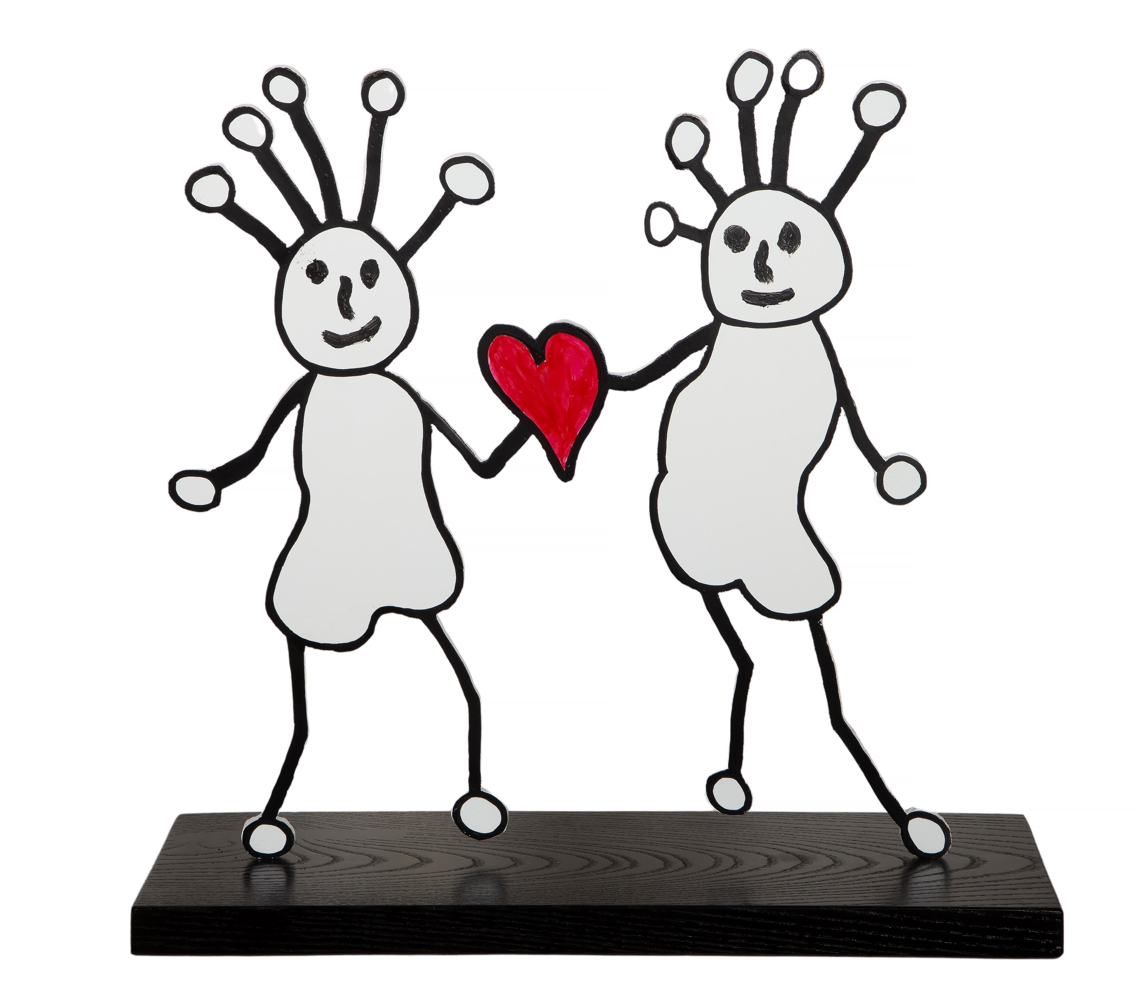 Una caprichosa escultura del artista pop y músico estadounidense Paul Kostabi. La escultura de metal y madera tiene dos caras y presenta dos figuras, delineadas con gruesas líneas negras, que sostienen un corazón rojo brillante entre ellas. Esta