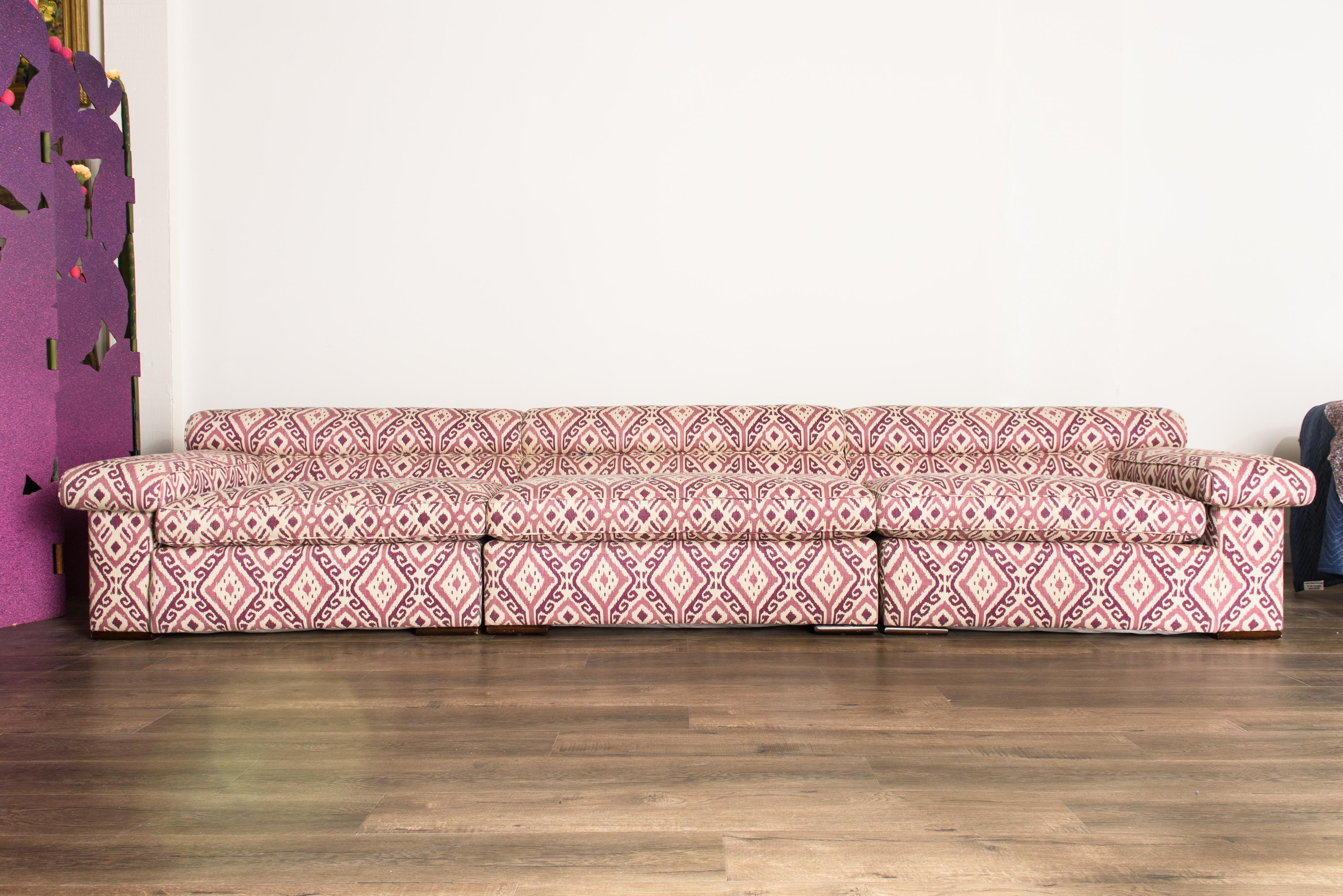 This modular lightly curved sectional sofa attributed to Paul Laszlo features three sections that can be arranged in several different ways, reupholstered in a gorgeous pink and plum colored ikat fabric which is in excellent like-new condition, only