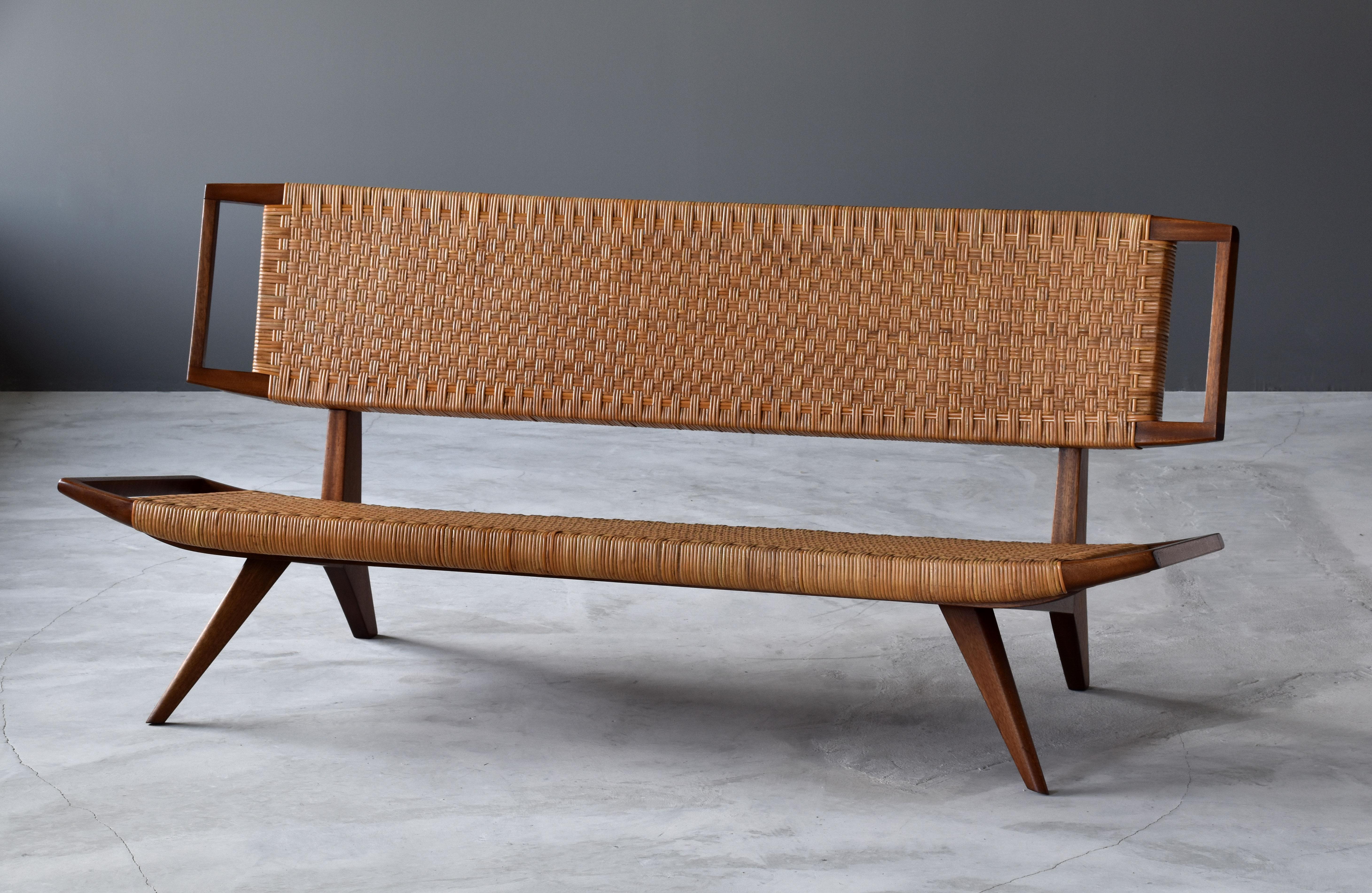 A sofa / settee / bench by Paul László for Glenn of California. Dark stained mahogany and original woven rattan / cane seat and back.

Paul László is considered among the most important California-based interior designer/architects of all time. At