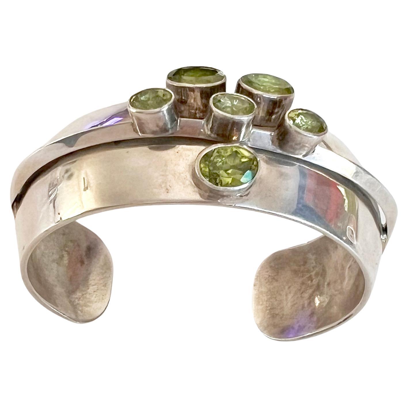 Argento 925 con sei pietre di peridoto autentiche sfaccettate create dall'artigiano Navajo Paul Livingston.  Il braccialetto ha una lunghezza totale da 6,75 a 7 pollici ed è largo 0,75 pollici.  Firmato Paul Livingston, Sterling.  In ottime
