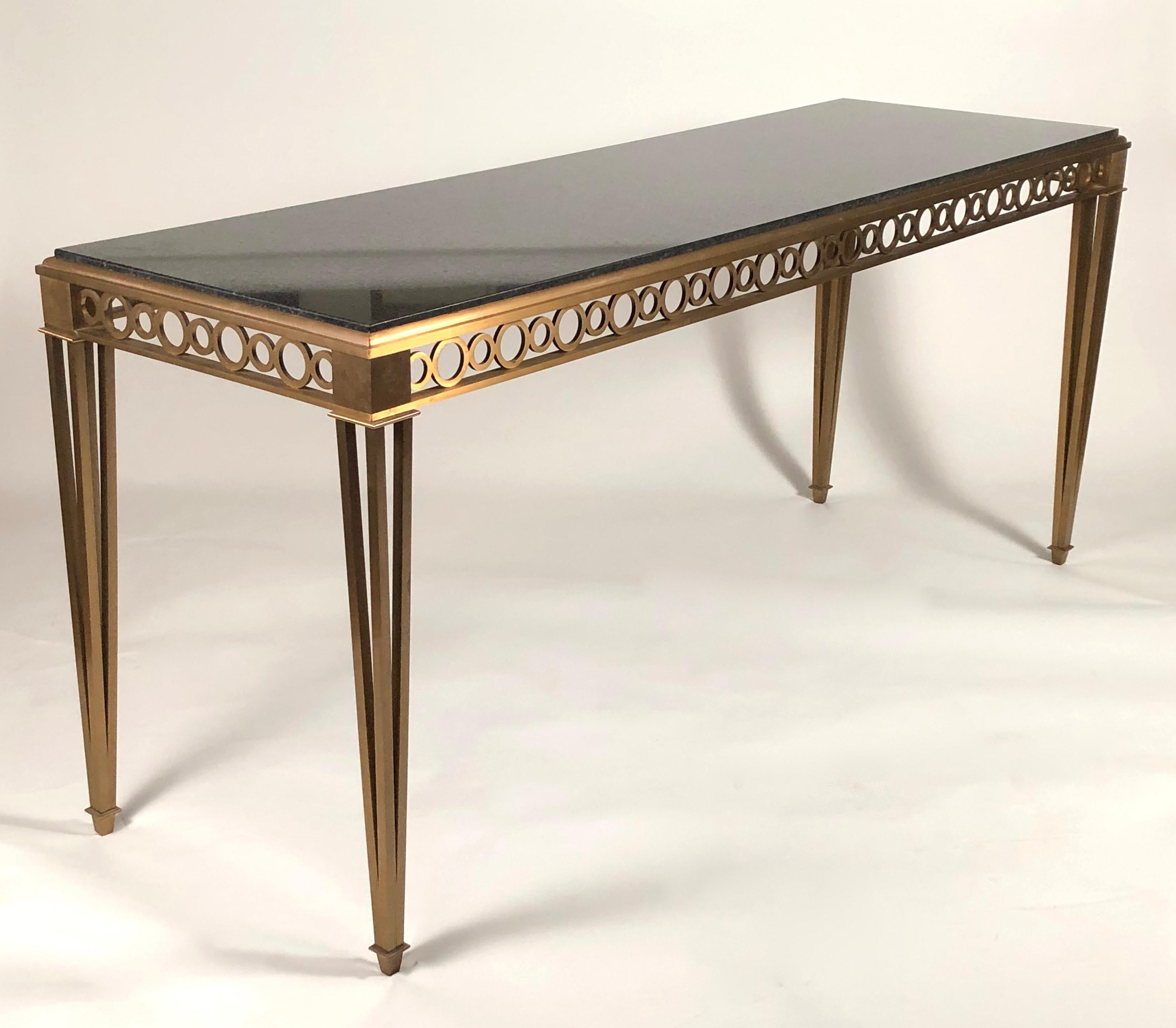 A chic and beautifully made solid brass and polished black granite console table attributed to Paul M. Jones, American, circa 1950-60, of rectangular form, the polished black granite inset top above a frieze of reticulated circles in alternating
