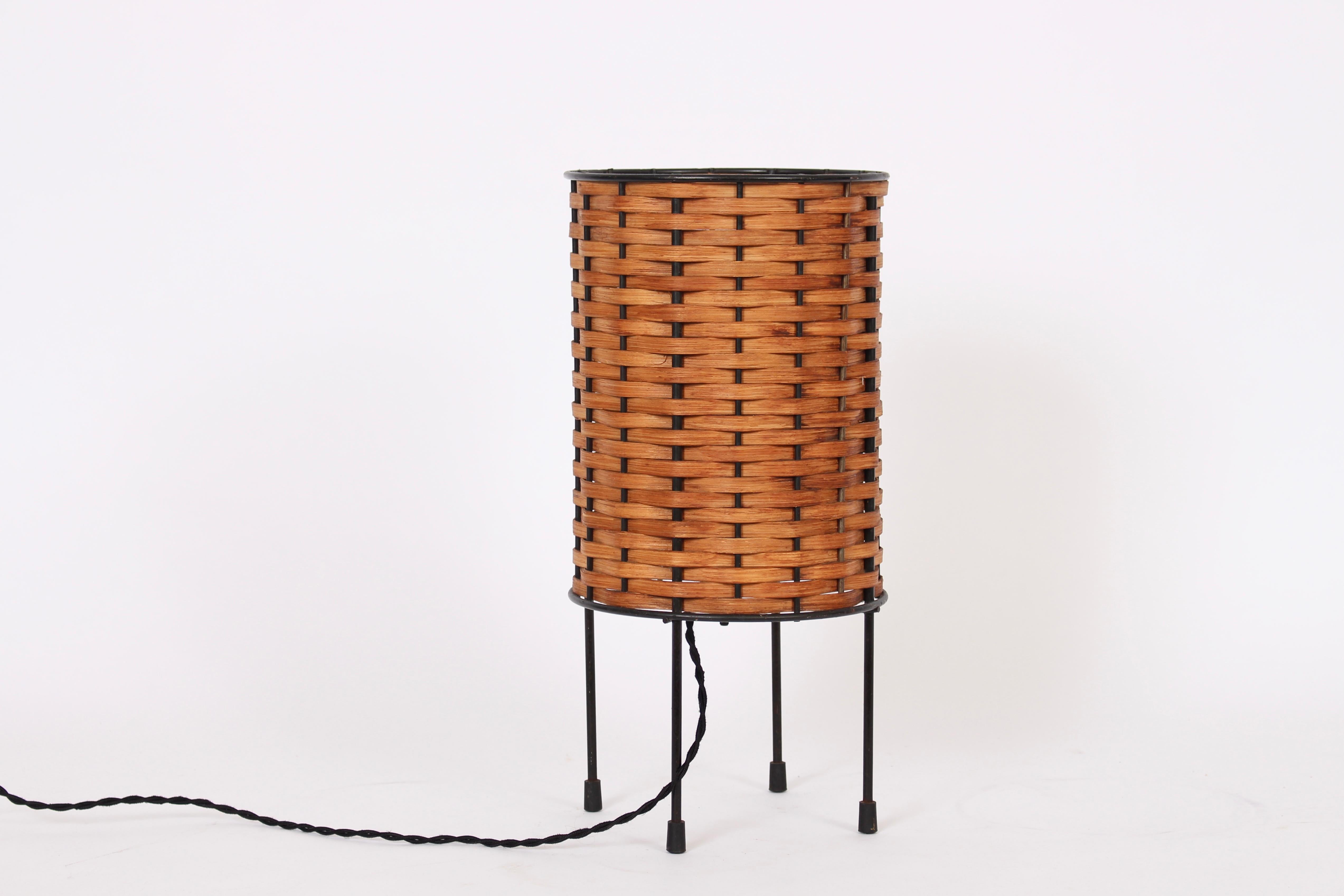 California Modern, Paul Mayen attributed, woven Oak Splint and Black Iron Wire Table Lamp. Featuring a cylindrical form, open Black enameled iron wire framework and tightly wrapped horizontal Oak weave on four wire legs detailed with capped feet.