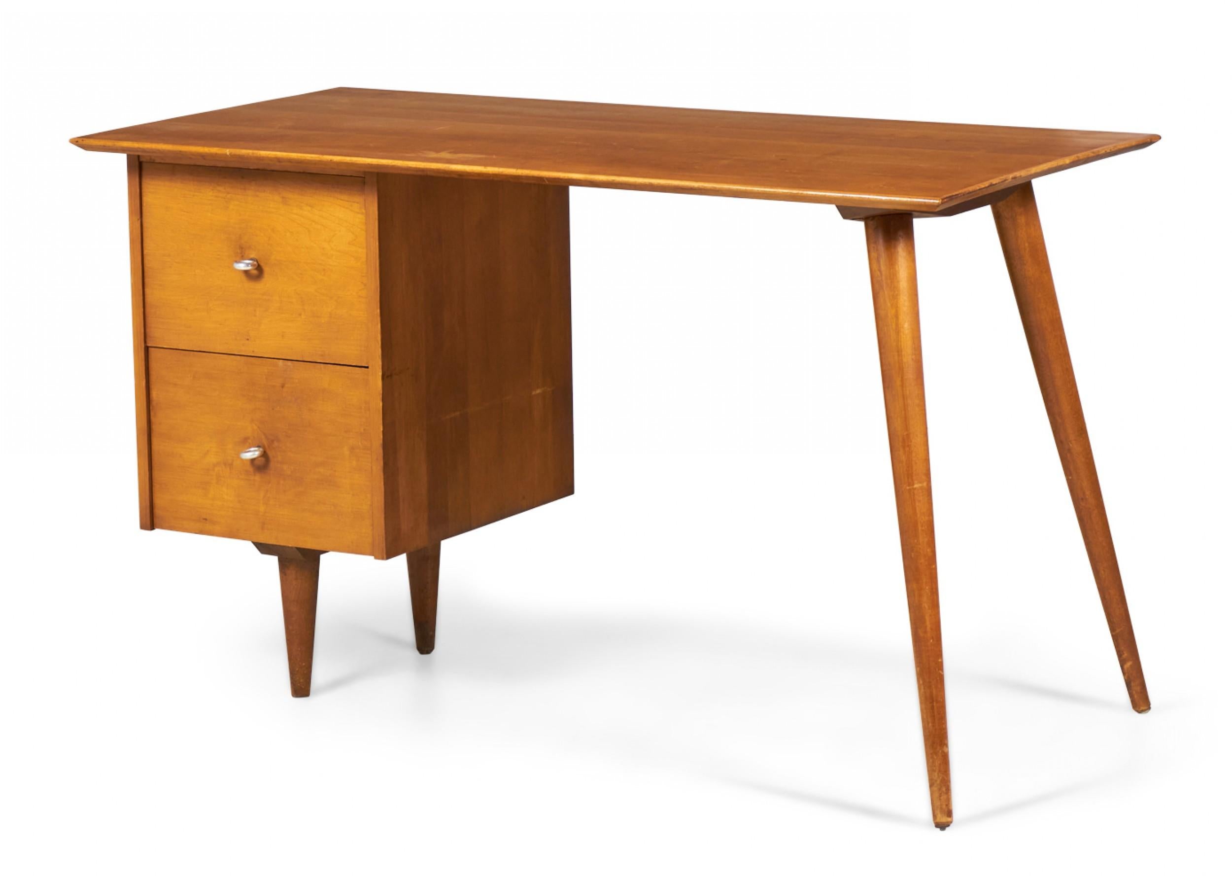 American Mid-Century blond maple student desk with a rectangular desktop supported on the left by two drawers with circular knob pulls resting on two short tapered legs, and on the right by two angled tapered legs. (PAUL MCCOBB, model 1560)(Same