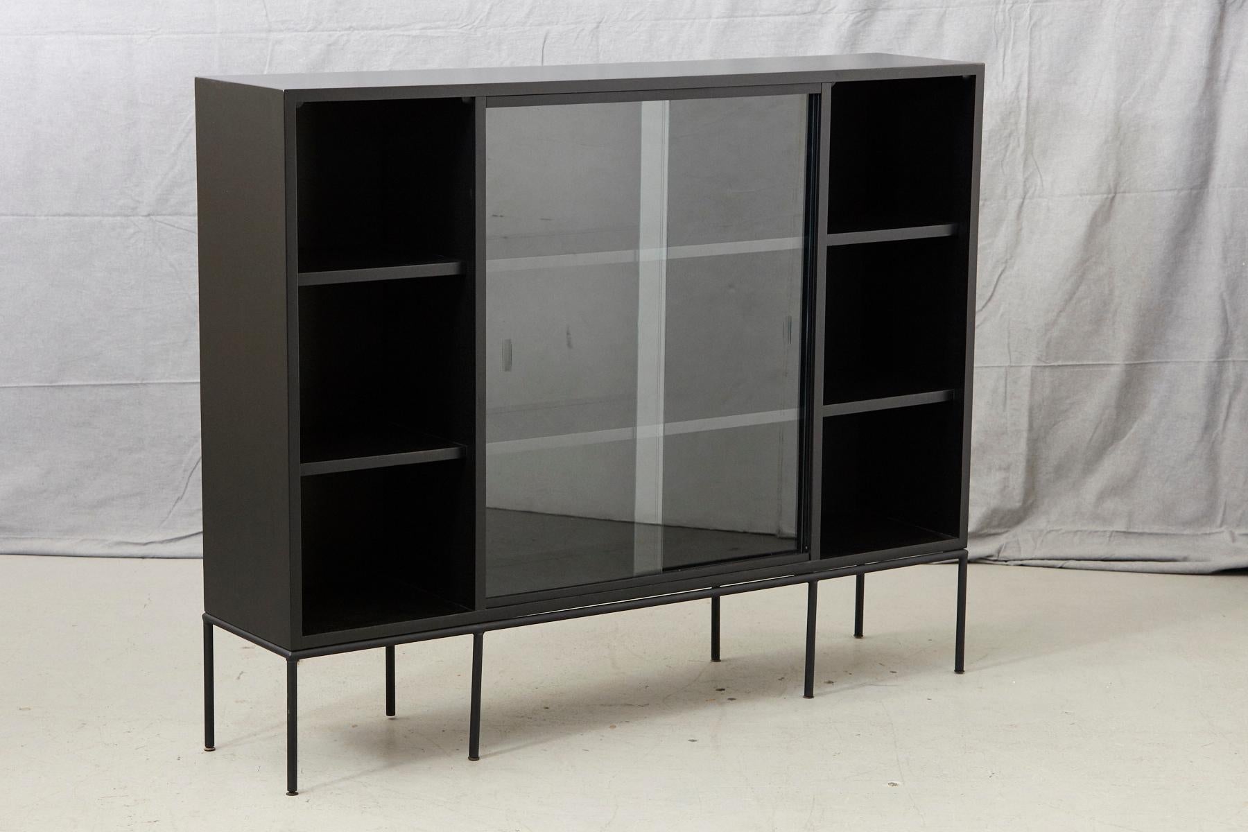 Paul McCobb for Planner Group, tall bookcase in new black finish with sliding glass doors mounted on an iron base, 1950s.
Very clean, pure, graphic lines, solid maple in new black finish. The sliding glass doors are removable.