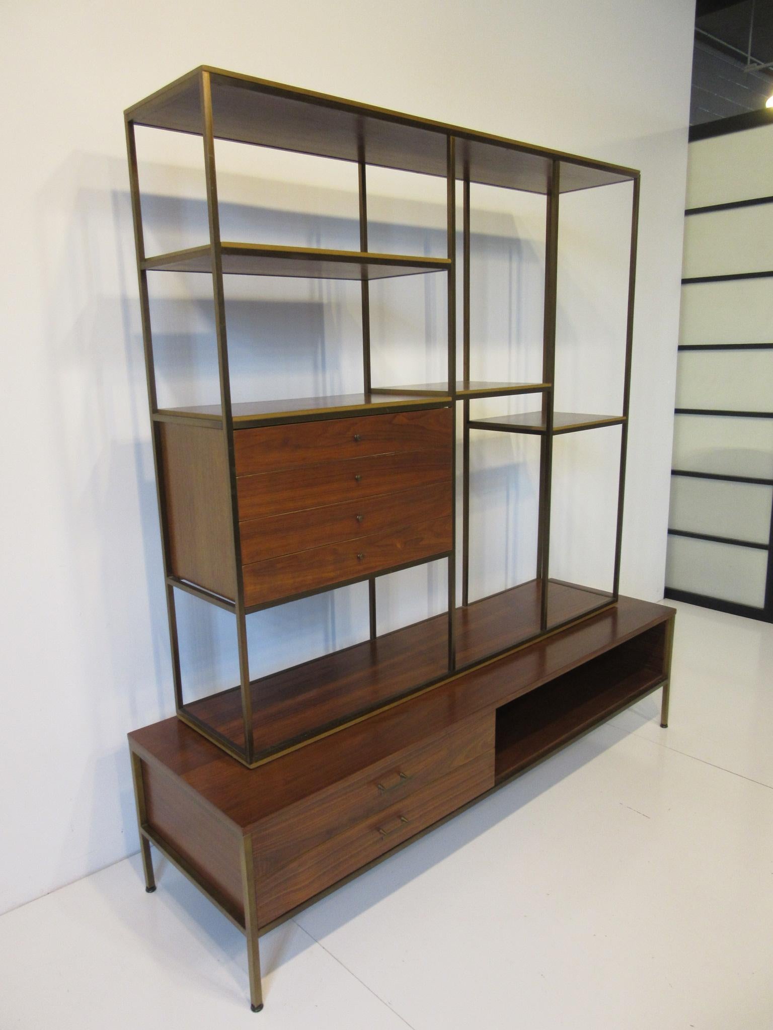 A well crafted two-piece brass frame and dark walnut bookcase / room divider with fixed shelves and four upper drawers with pulls . The lower base has a brass frame and two longer drawers with handles and a storage area to the other side . The piece