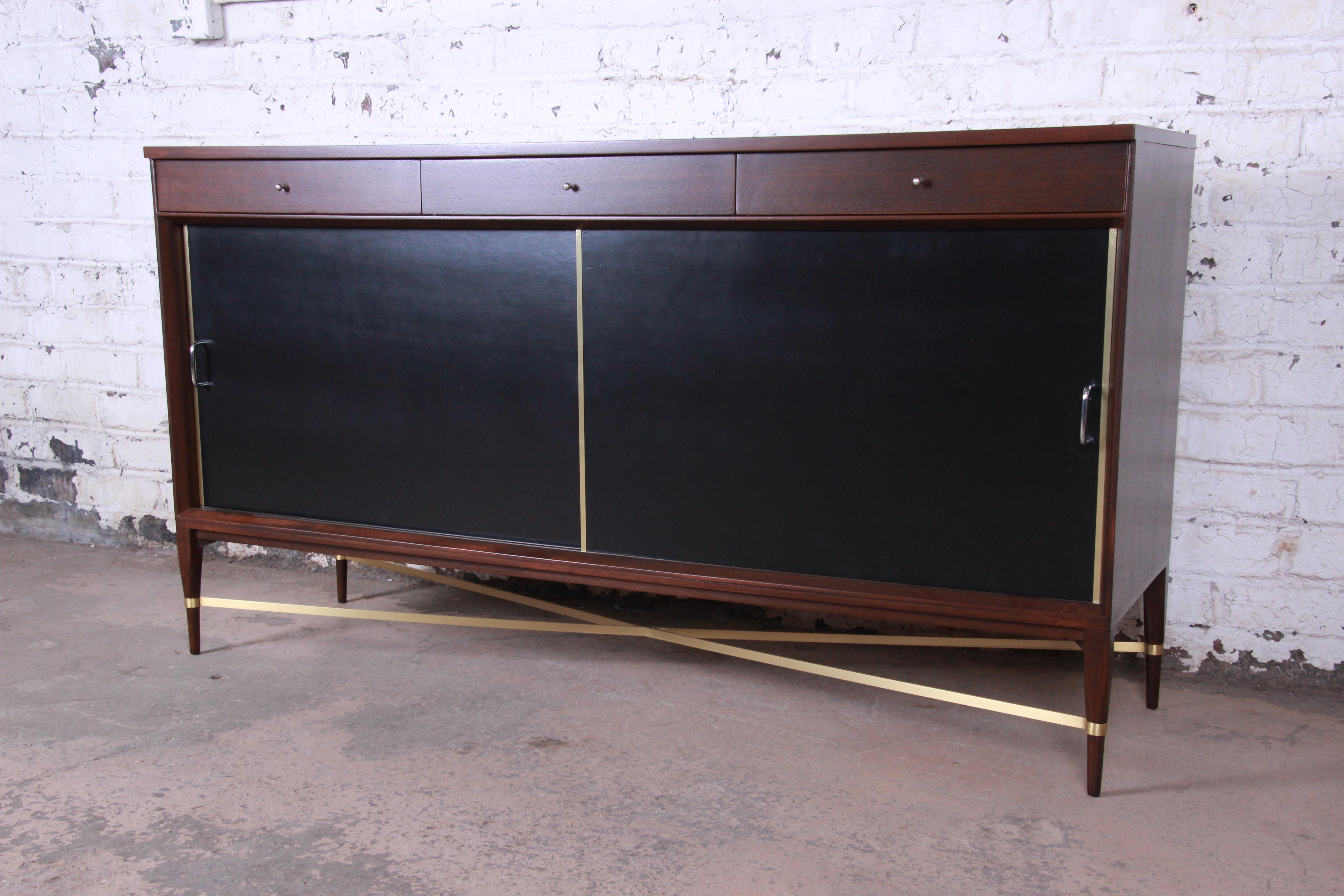 An exceptional Mid-Century Modern mahogany and brass sideboard credenza designed by Paul McCobb for his Calvin Group Collection for Calvin Furniture. The credenza features gorgeous mahogany wood grain and unique X-base brass stretchers. It offers
