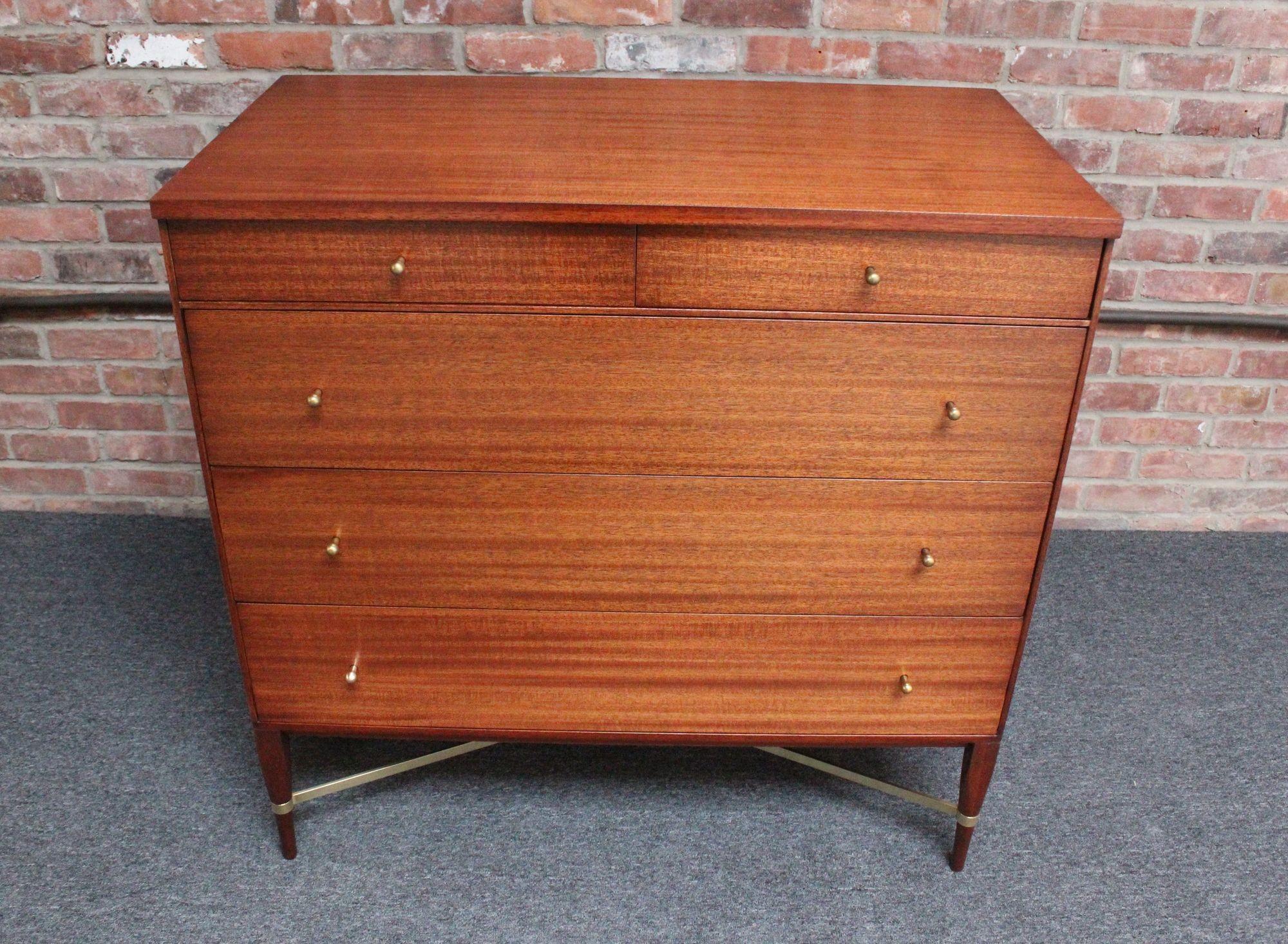 Paul Mccobb Calvin Group five-drawer chest (model 1003) manufactured by Directional Furniture (ca. early 1950s, USA).
Composed of a stained mahogany chest with brass tear-drop pulls supported by carved, tapered legs and brass 'x' stretchers.