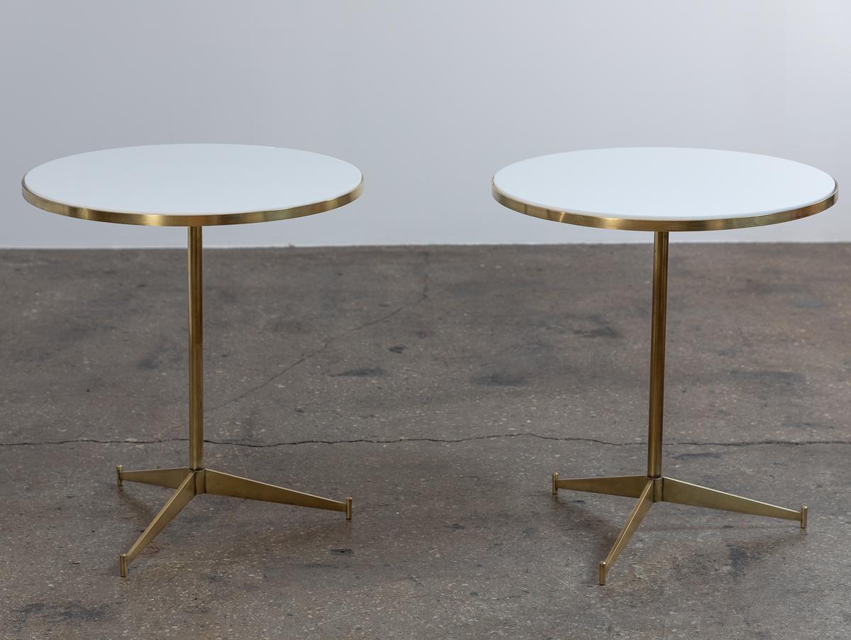 Pair of occasional tables, model no. 1094, designed by Paul McCobb for Directional.  Graceful pedestal base is elevated on three angular legs. Round table top is fitted with the original white Vitrolite glass, which has a beautiful opalescent