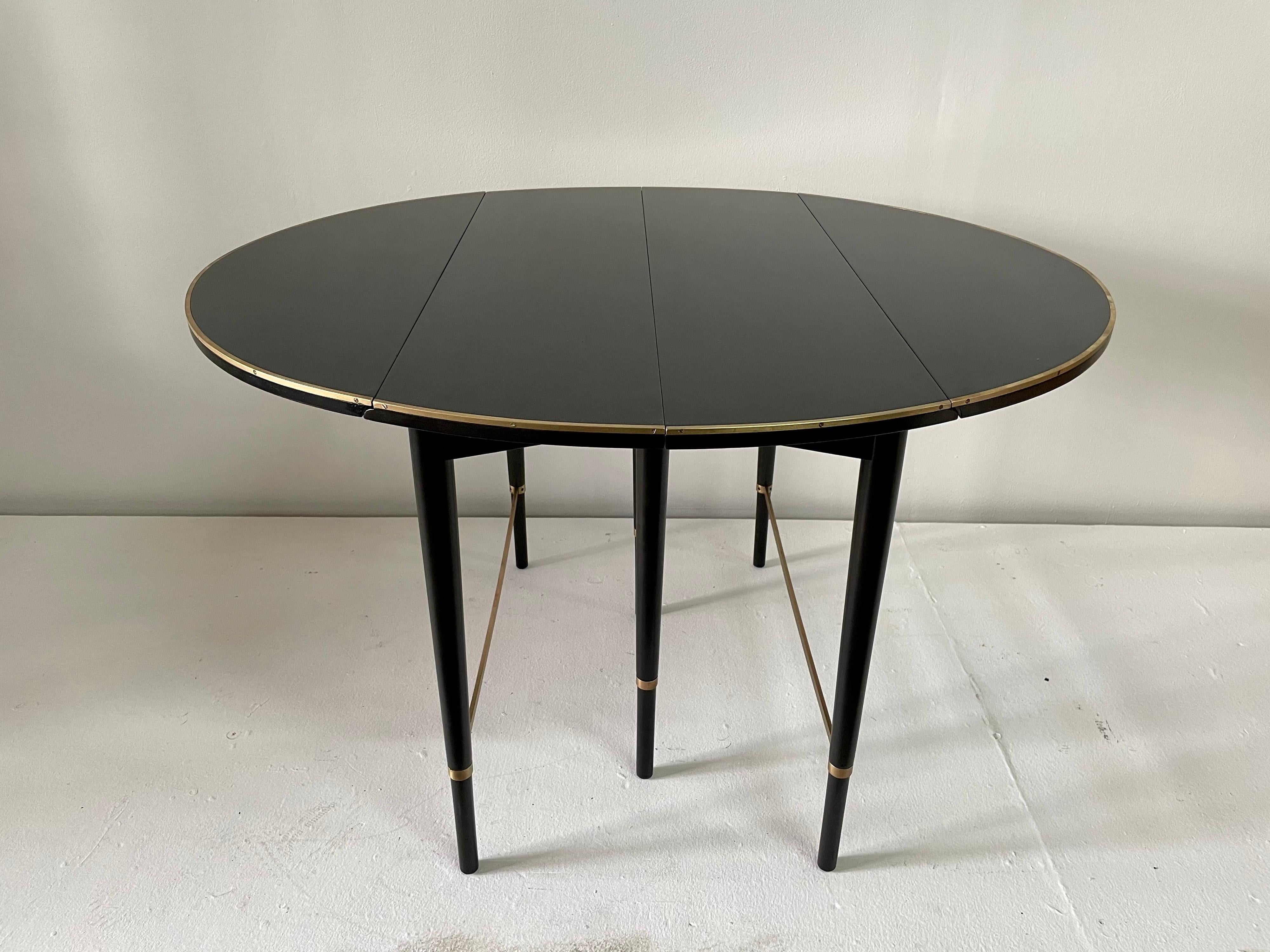 In exceptional vintage condition this 4 leaf extendable ebonized mahogany dining table with brass stretchers and trim is designed by Paul McCobb for H. Sacks & Sons 