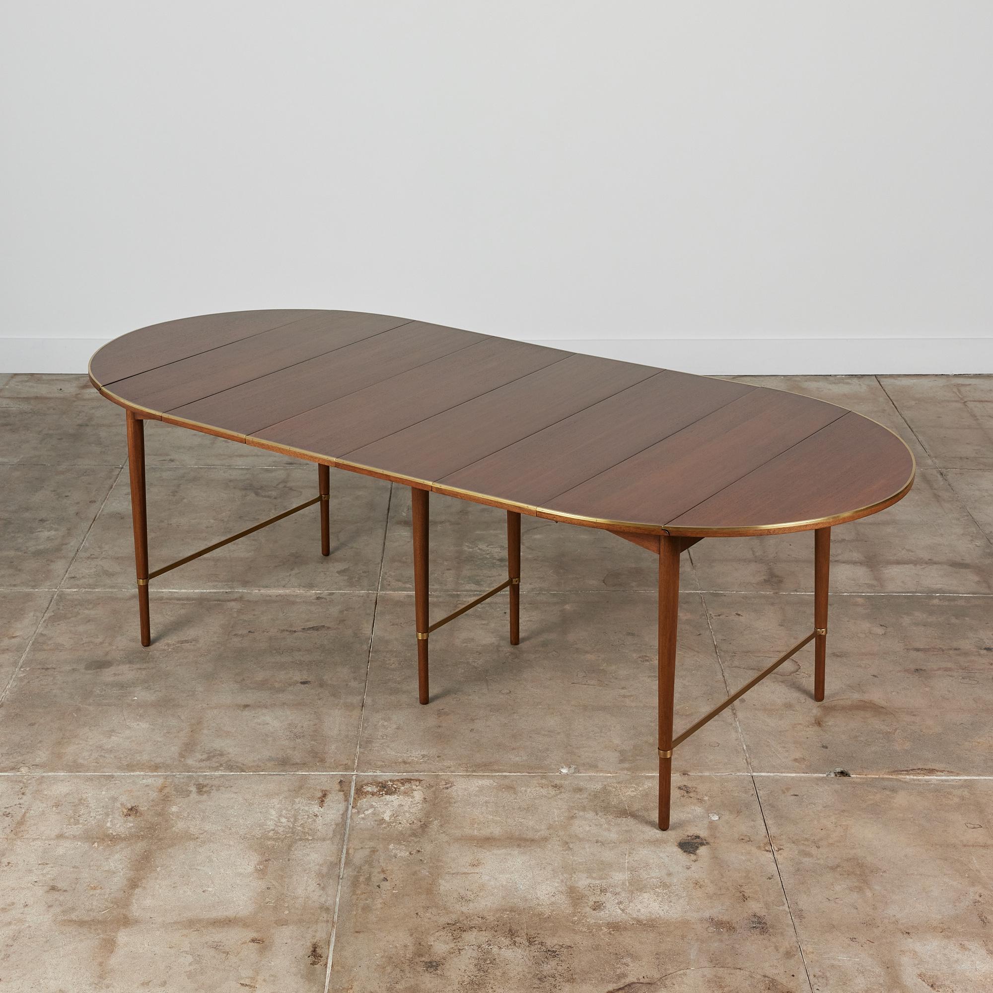 Designed by Paul McCobb, circa 1950s, USA for H. Sacks & Sons “Connoisseur” line. This walnut table features an oval table top when fully extended. The edge of the table showcases a beautiful brass trimming. The tables six tapered legs are supported