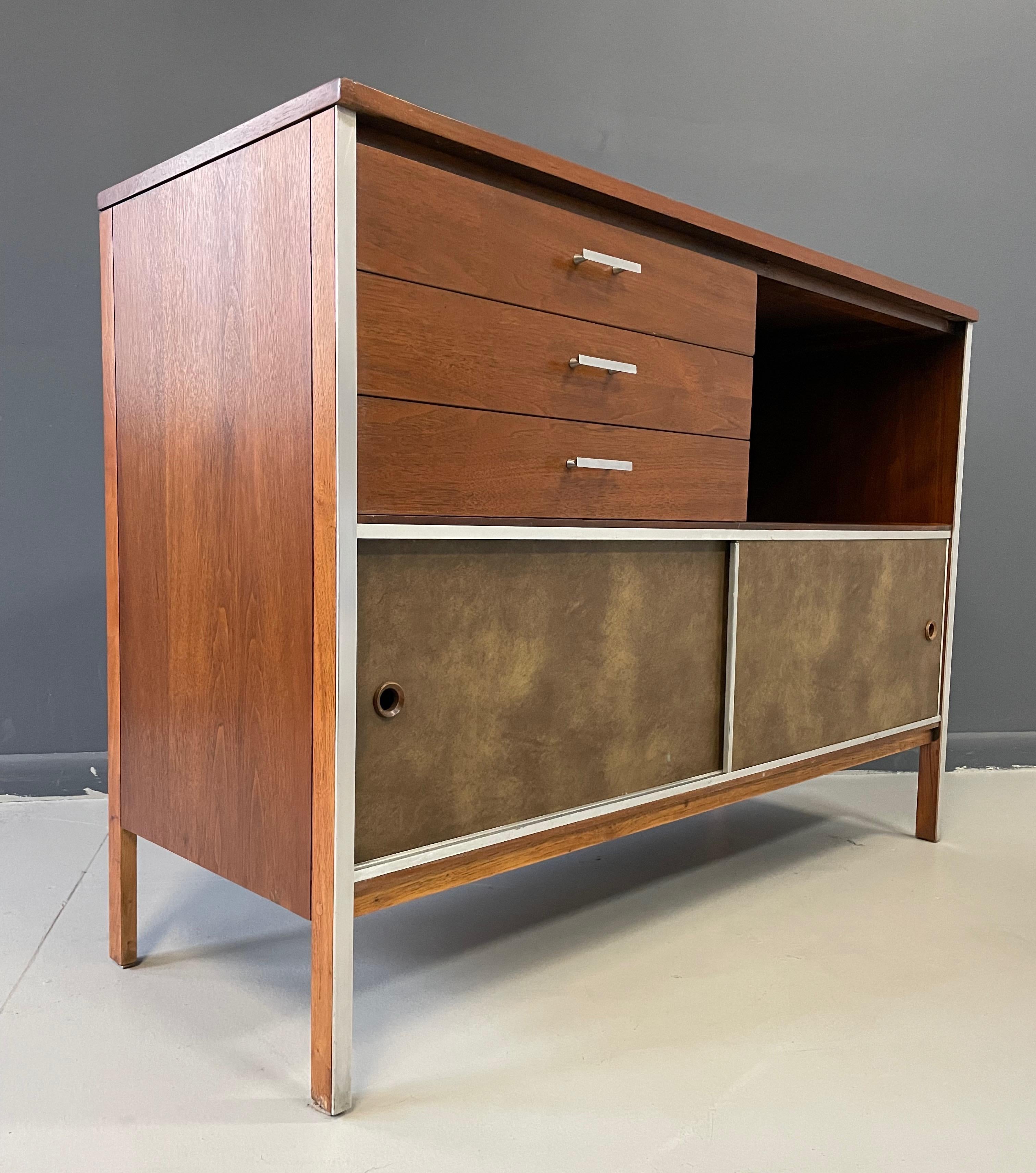 Paul McCobb for Calvin Furniture Linear Group credenza in walnut and aluminum. Constructed of two lower textured leatherette sliding doors in front of two divided open interior compartments / three drawers at upper left side with original aluminum