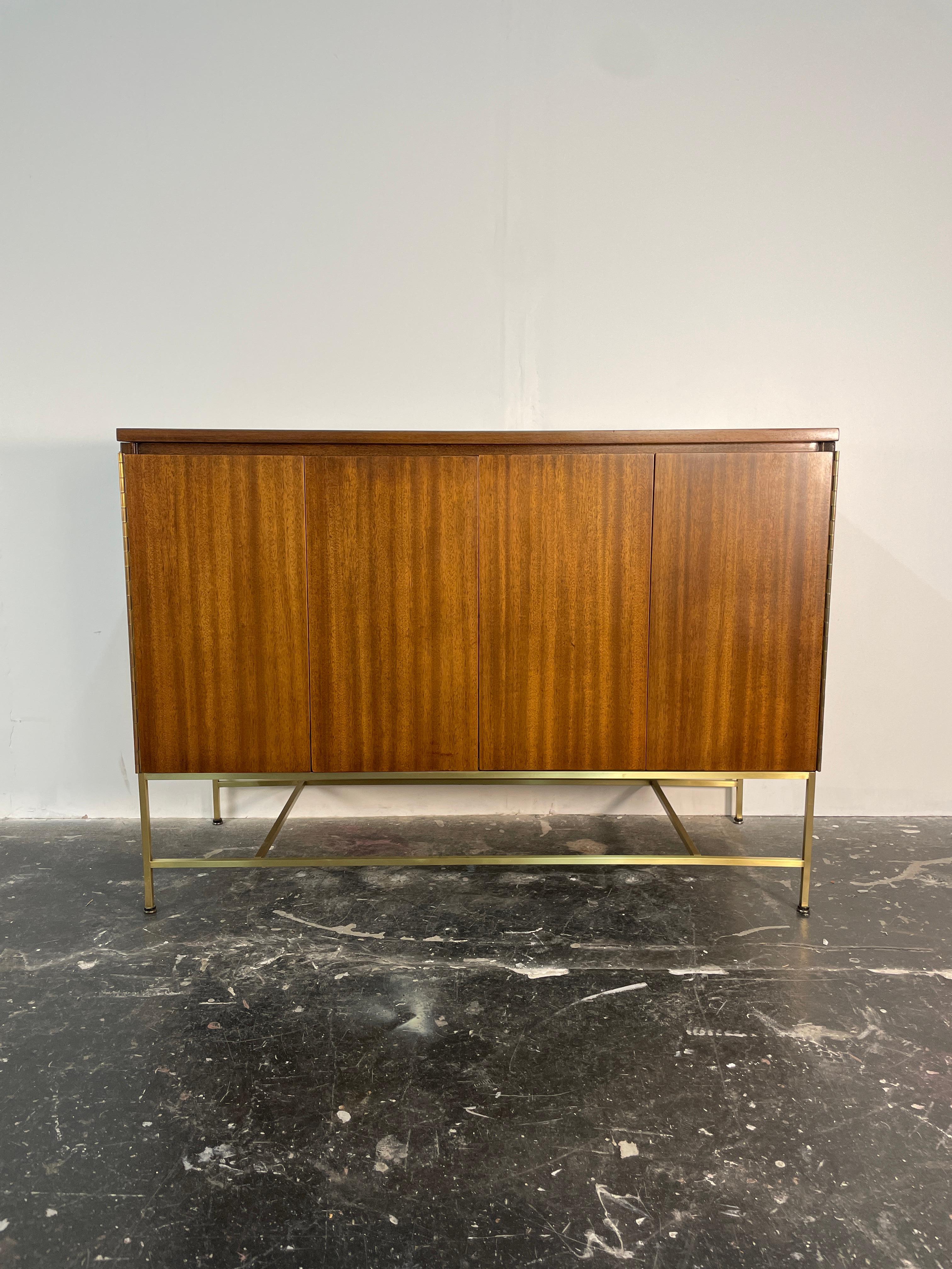 A vintage mahogany and brass credenza server has mahogany bi-fold doors and brass legs. Created by the iconic Mid-Century Modern American designer,Paul McCobb for the Calvin Group.

This case piece features mahogany doors that swing open to a