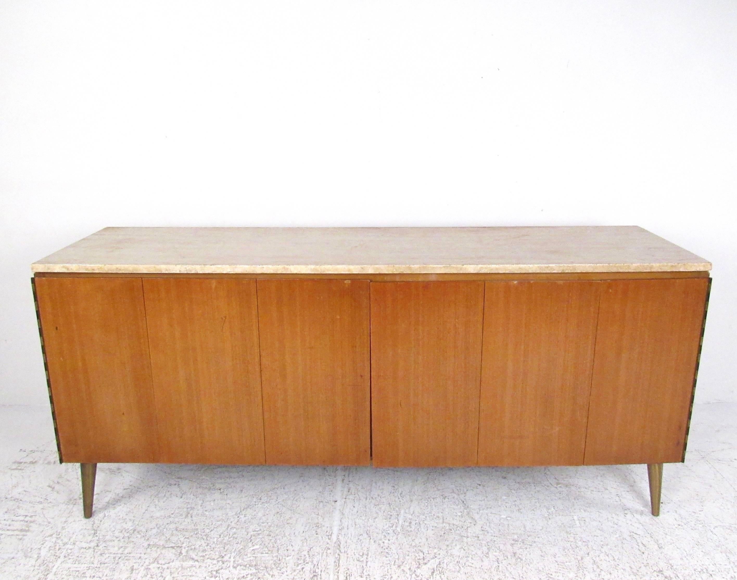Questa elegante credenza di metà secolo presenta l'iconico design di Paul McCobb e vanta una finitura vintage in mogano e un sorprendente piano in travertino. Le gambe affusolate in ottone aggiungono fascino a questa credenza moderna americana