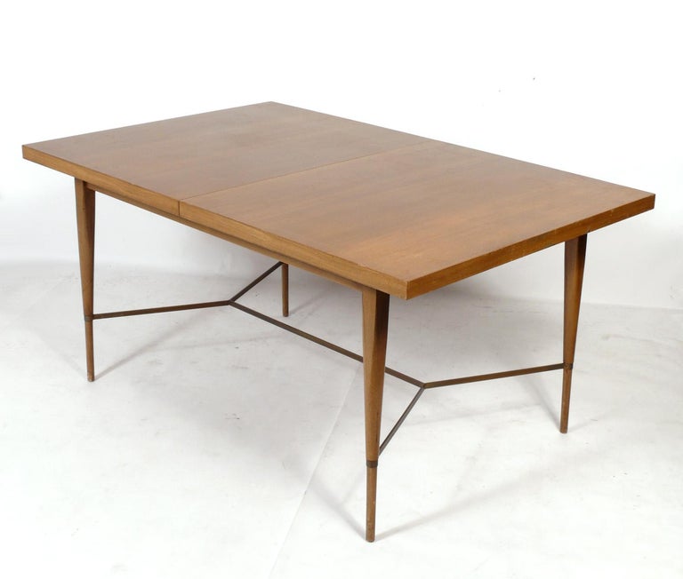 Paul McCobb dining table for Calvin, American, circa 1950s. Elegant design with brass stretcher. This table is currently being refinished and can be completed in your choice of color. The price noted INCLUDES refinishing in your choice of color.