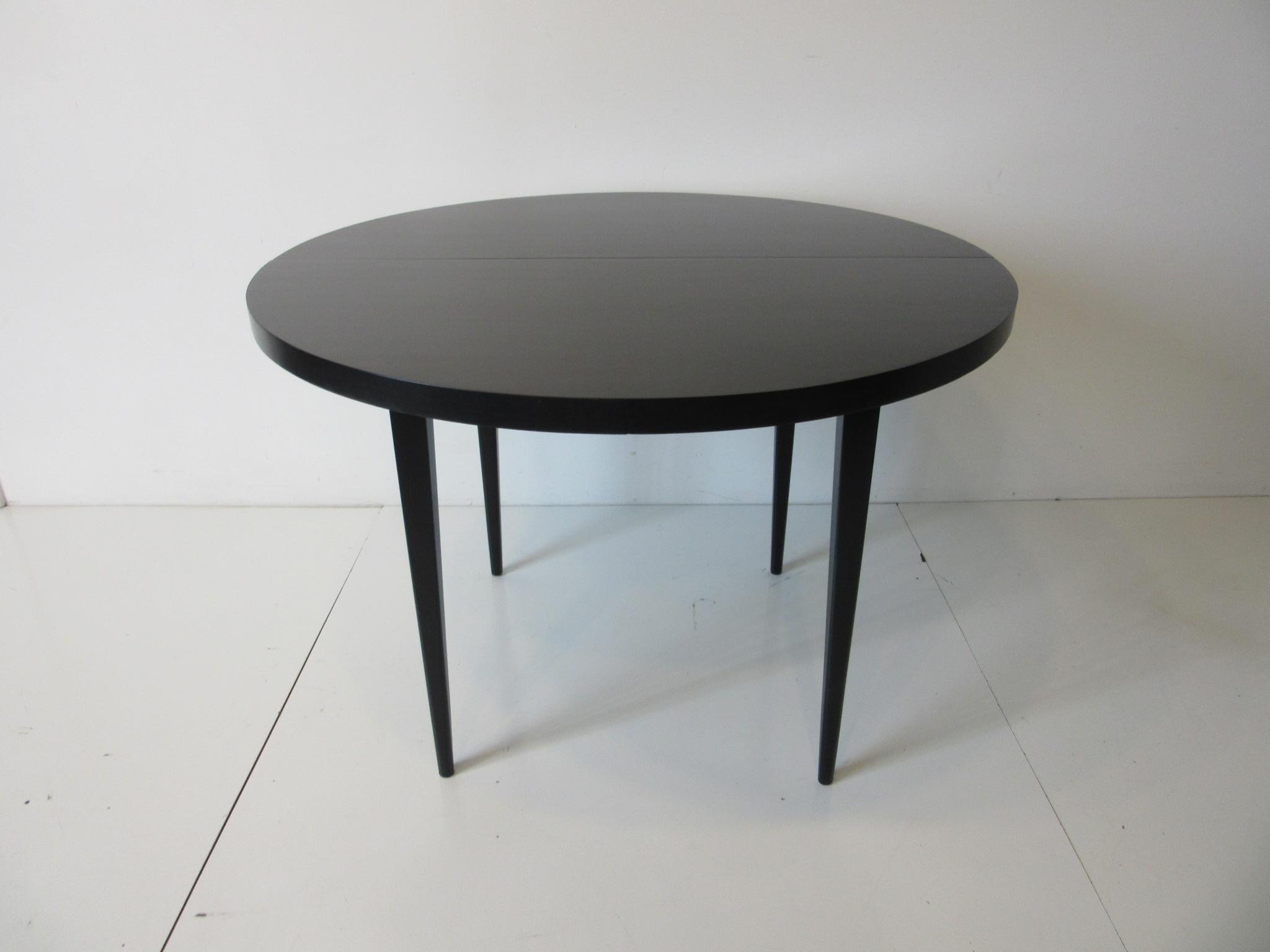 A solid maple wood midcentury dining table in satin black with two 15