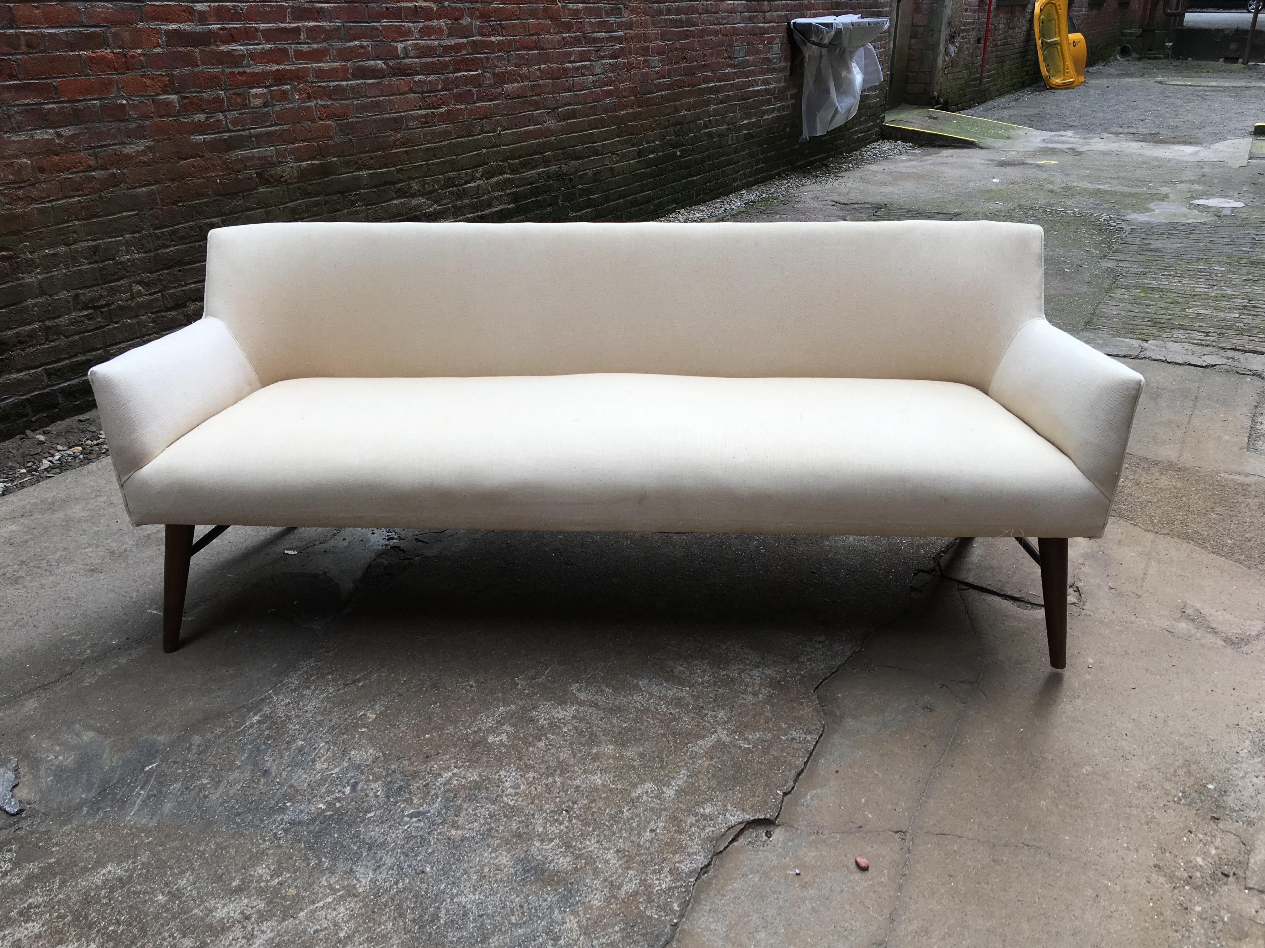 Elegant and refined profile Paul McCobb tub sofa design for Directional. Upholstered seat and back resting on tapered dowel legs with a cross stretcher base. Re-upholstered in the 1980s with a heavy duty white canvas duck cloth.