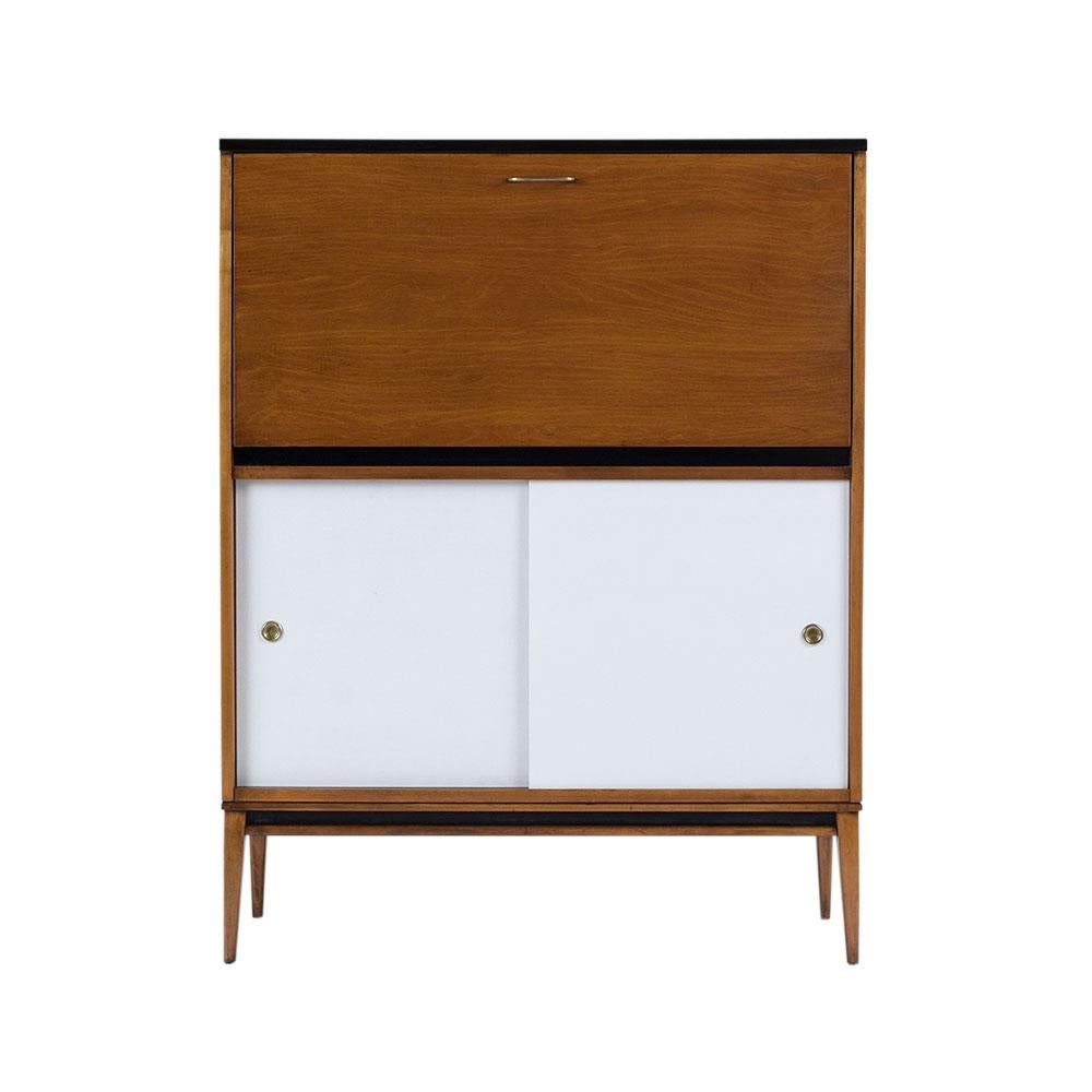 This drop front desk by Paul McCobb planner group has been professionally restored, is made out of maple wood, and features a multi-color stain combination with a newly lacquered finish. This piece comes with a drop front desk with a brass handle,