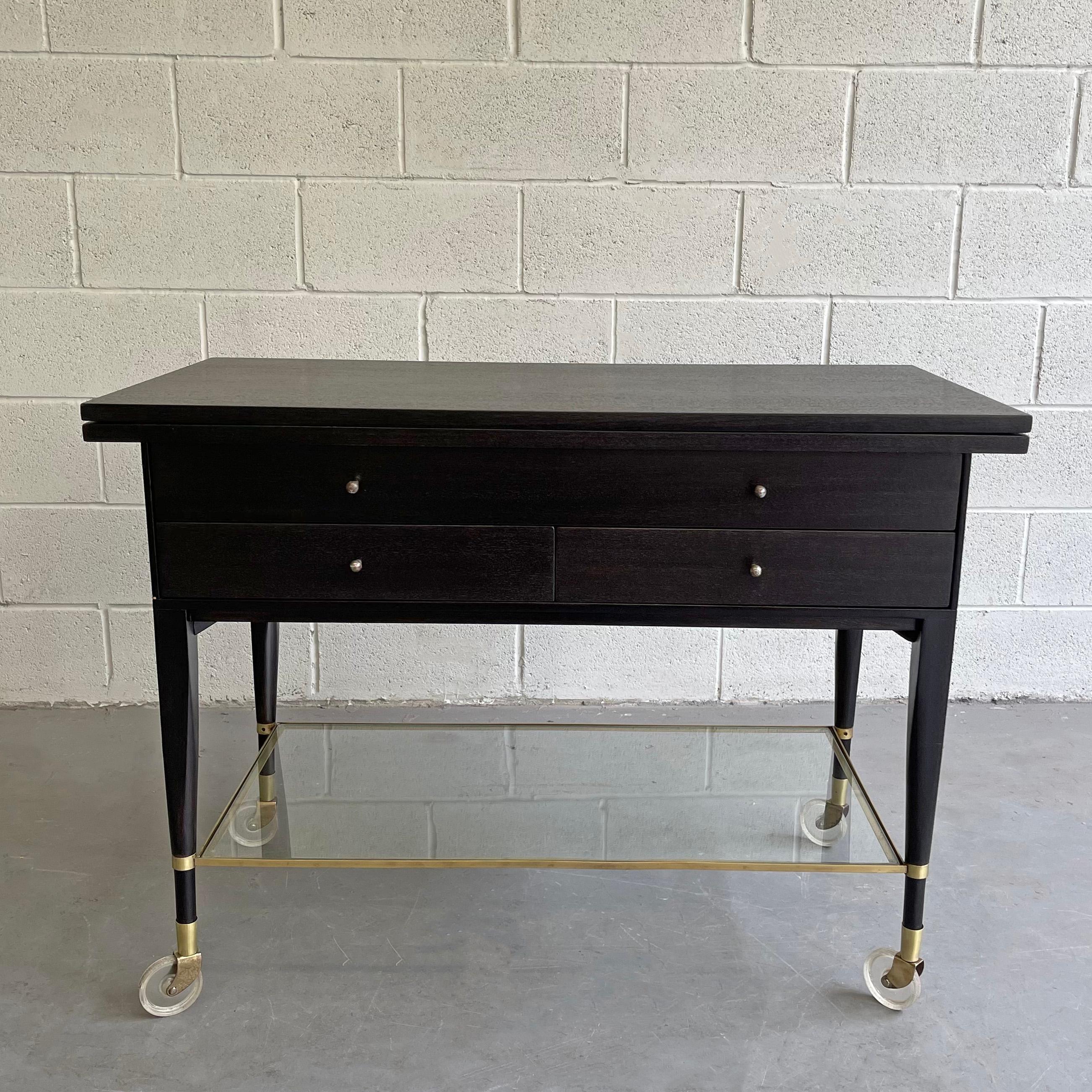 Mid-Century Modern, 4 drawer, mahogany, extension, bar or serving cart by Paul McCobb for Calvin Furniture features an ebonized finish with brass details and hardware and glass lower shelf. The top flips open to extend to 80.5 inches.