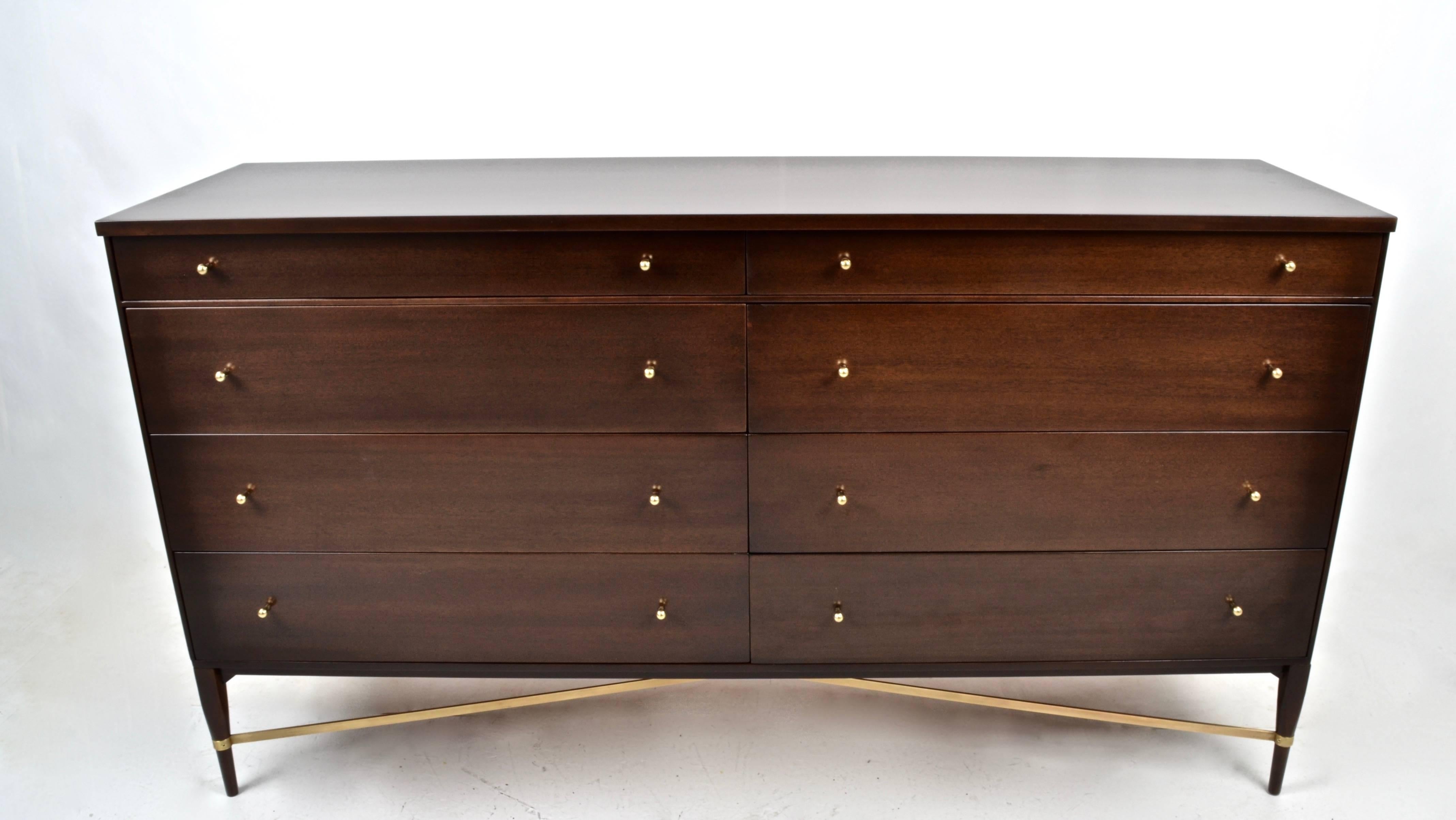 Fully restored in dark walnut stain, McCobb eight-drawer dresser with distinctive brass cross stretcher. Original brass hardware. Solid construction, clean drawer interiors. Designer and manufacturers label still affixed.