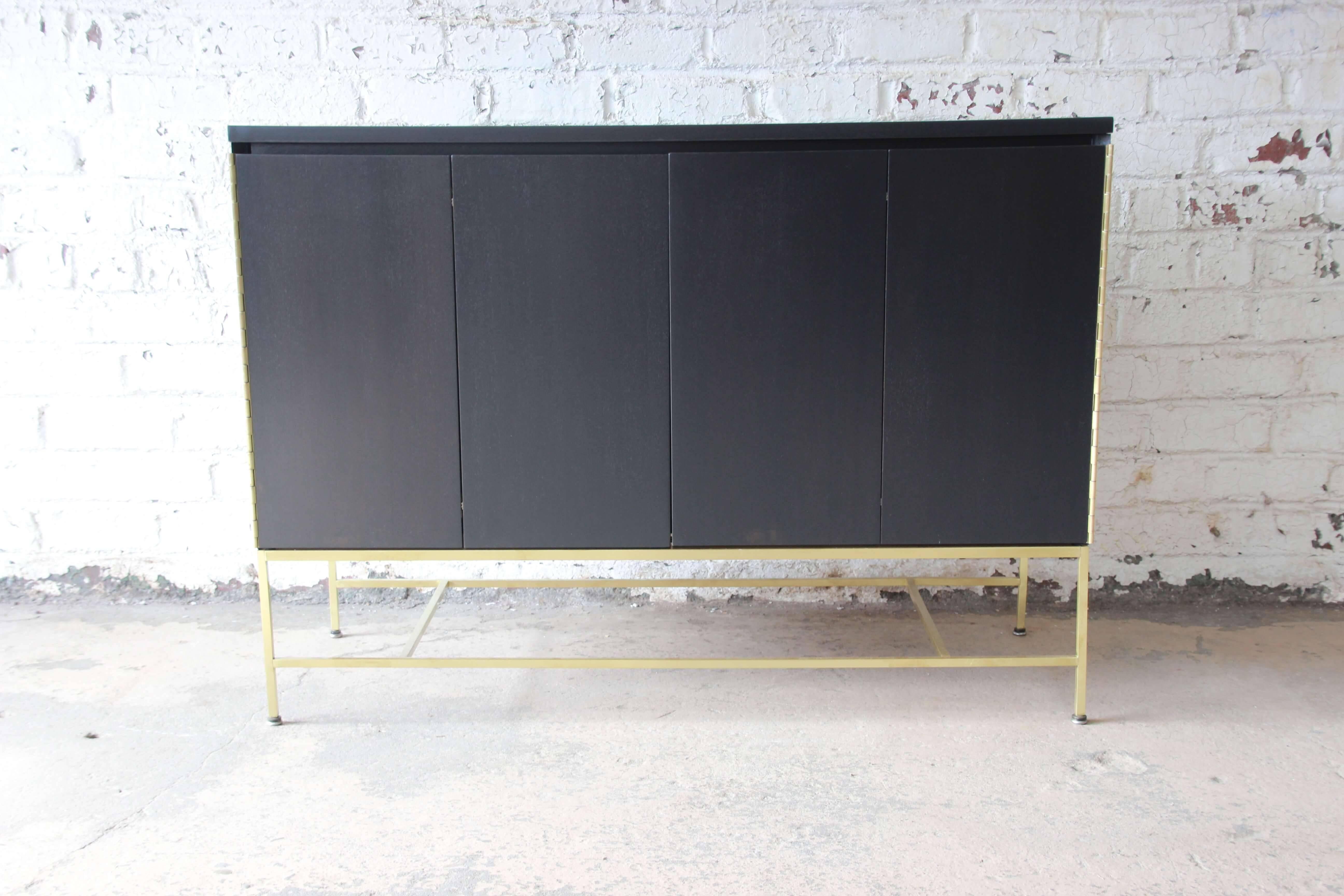 Offering a superb newly refinished ebonized Paul McCobb sideboard credenza for Calvin furniture. This piece has a beautiful ebonized finished with polished brass base. There are bi-fold doors on each side opening to a drawer on adjustable shelf on