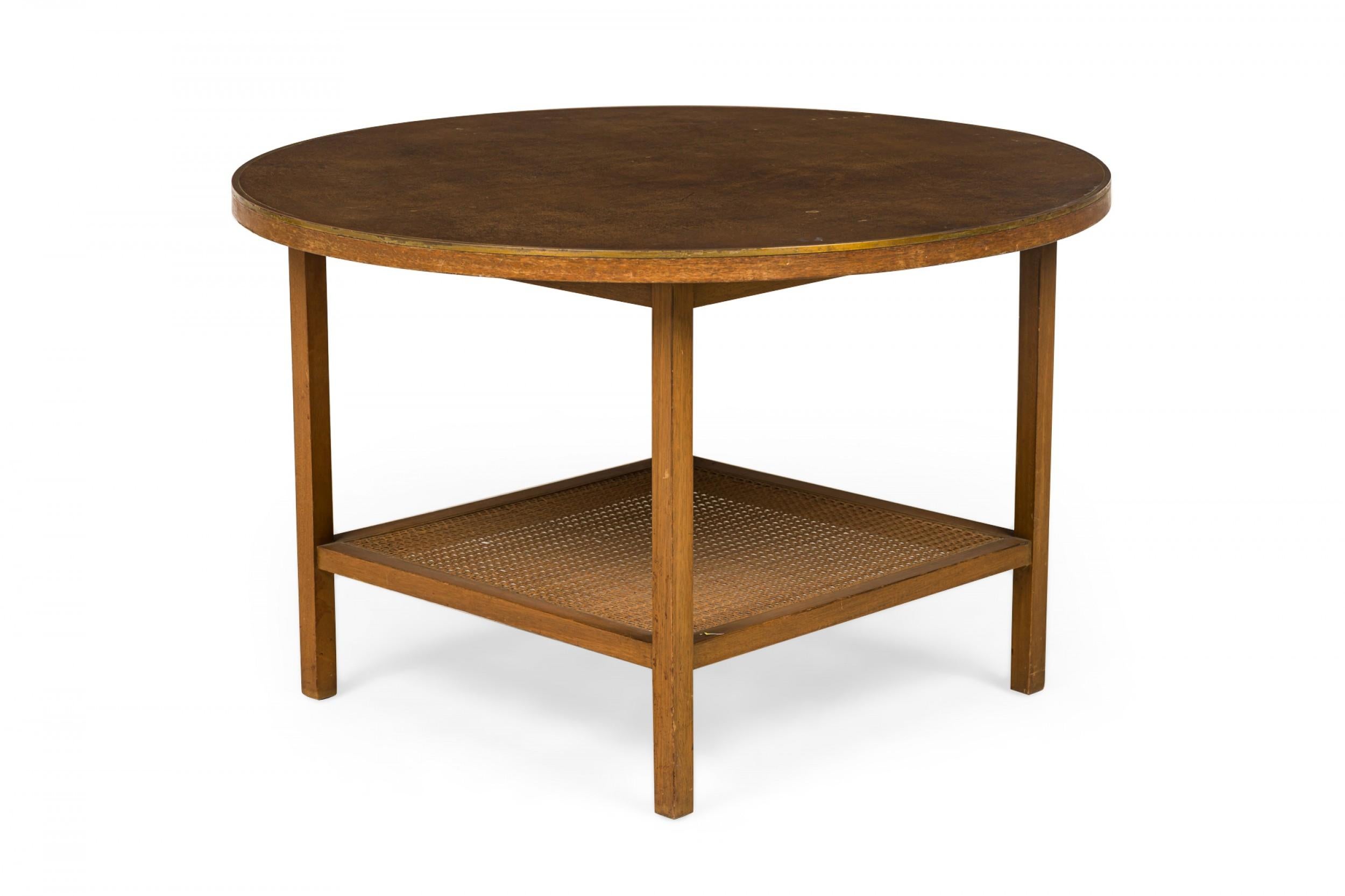 American Mid-Century end / side table with a round leather top trimmed in brass, resting on four square wooden legs with a lower square caned stretcher shelf. (PAUL MCCOBB FOR CALVIN FURNITURE COMPANY).