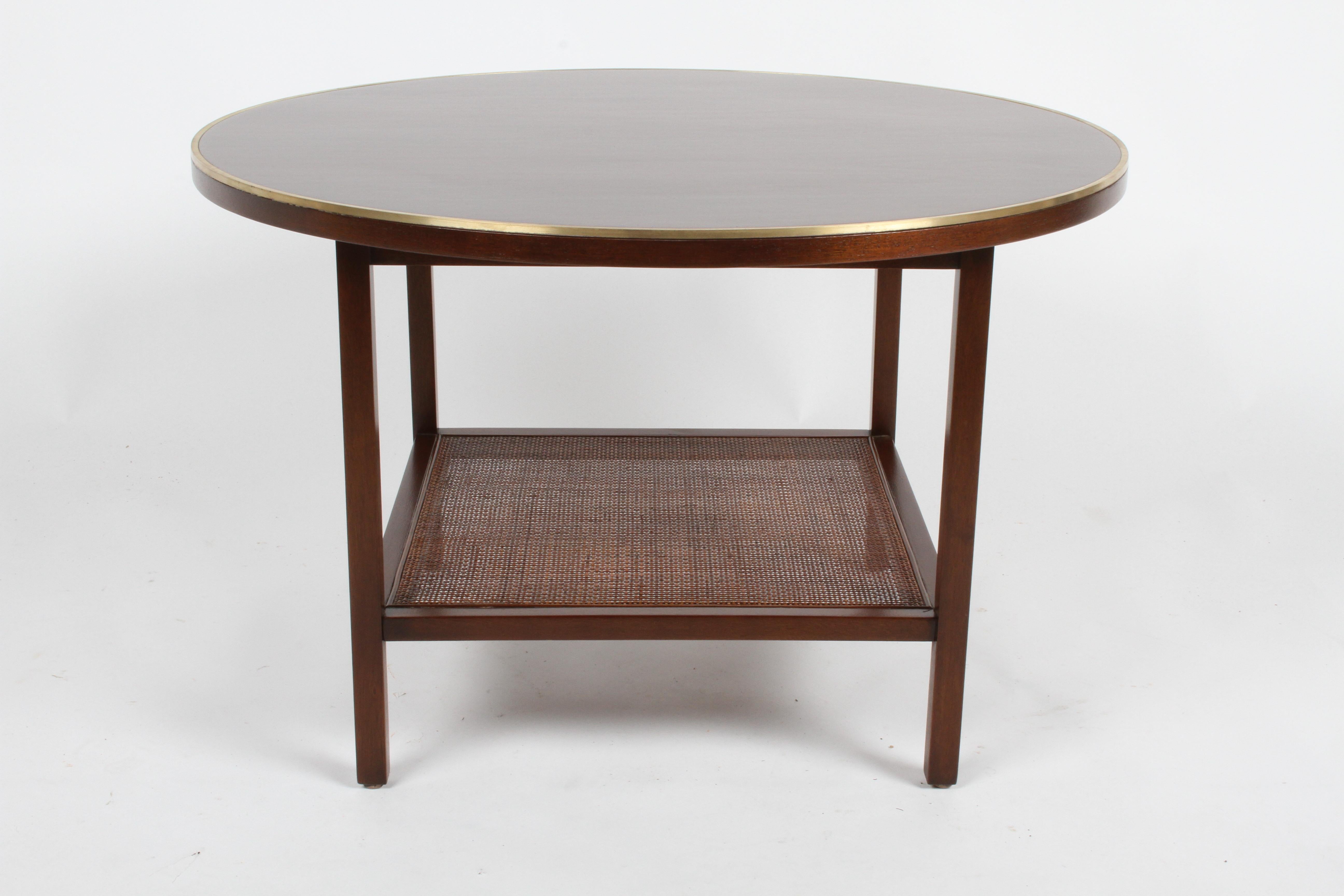 Restored Paul McCobb for Calvin model 8734 round side or end table with Mahogany top, having brass trim edge with lower wicker shelf. Refinished in a medium brown walnut stain, re-glued and polished brass trim. Label.