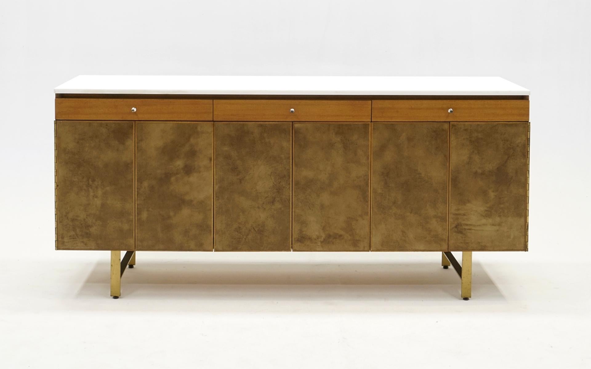 Credenza / sideboard / buffet / media cabinet designed by Paul McCobb for Calvin.  Mahogany case with three drawers, sturdy brass legs, leather covered trim-fold doors revealing adjustable shelves and a 1/2' thick milk glass / Vitrolite top.  This