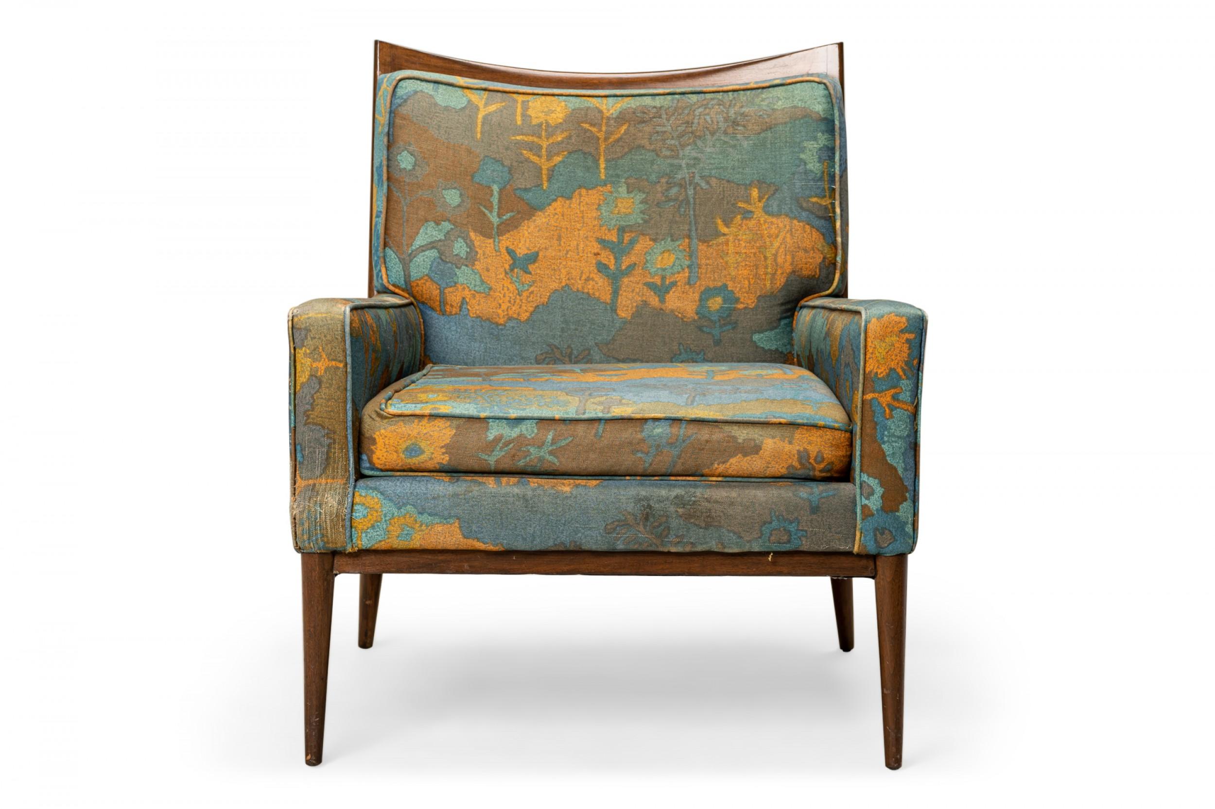 American mid-century lounge / armchair with a walnut frame with a scooped back rail and blue, orange, and brown floral patterned fabric upholstery, resting on four tapered dowel legs. (PAUL MCCOBB FOR DIRECTIONAL)
