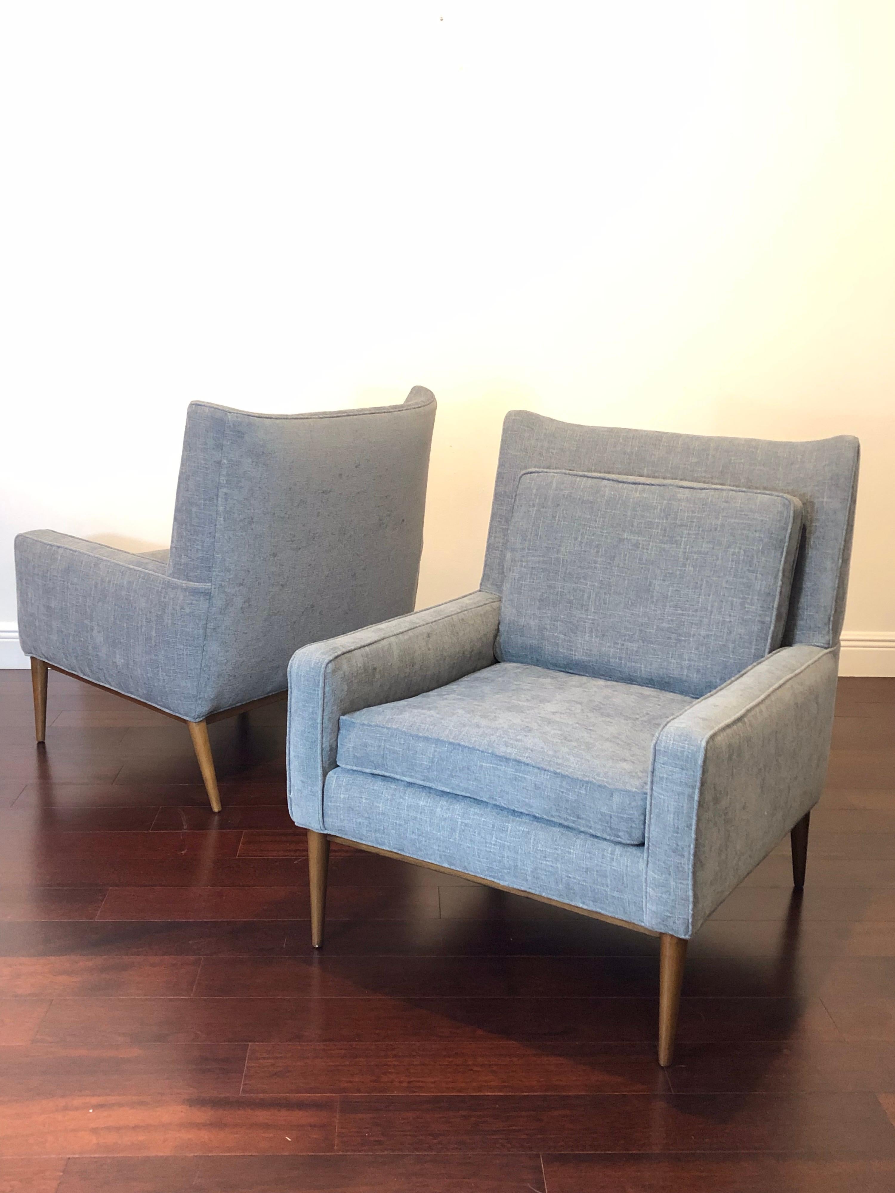 Wonderfully restored pair of Paul McCobb lounge chairs, model 1312. Upholstered in a steel grey with a small blue hue. Mahogany legs refinished in a walnut tone. New foam. These are a fine example of Mid-Century Modernism, with elegant tapered legs,